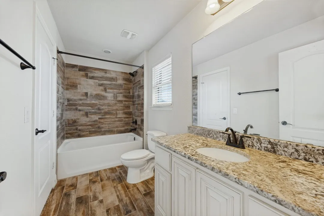 Bathroom featuring a tub/shower combination with stacked tile surround, wood-finish flooring, a single vanity with stone countertop, and an integrated sink
