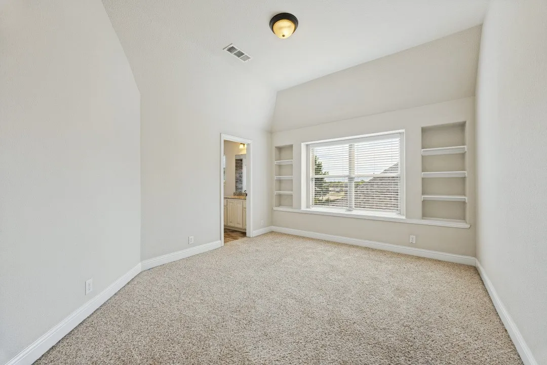 Sloped ceilings, neutral-toned carpet flooring, built-in shelving, and a prominent window with blinds