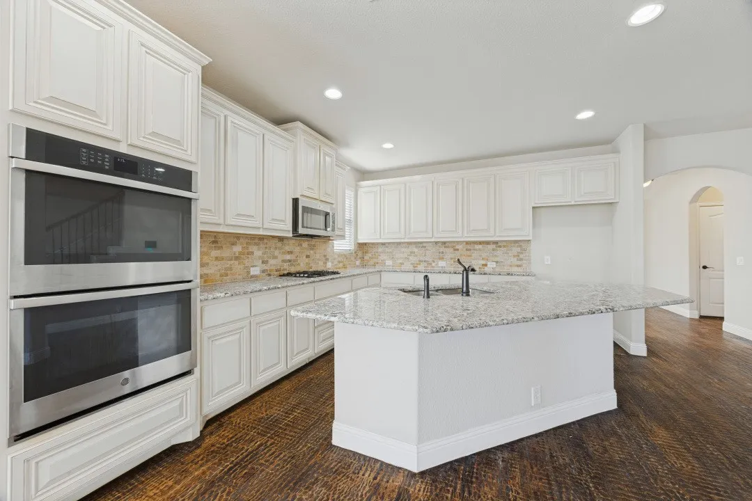 Kitchen featuring an island, white cabinetry, granite countertops, tile backsplash, and wood-finish flooring