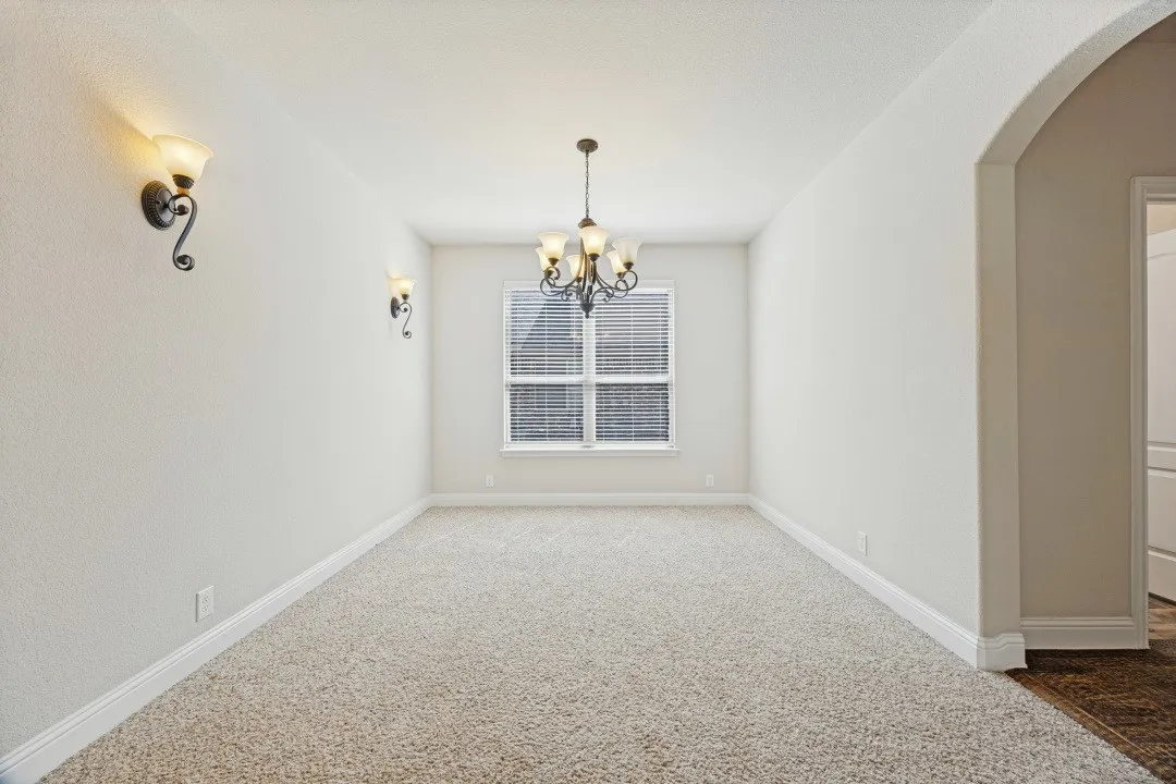 Neutral tone wall paint, carpet flooring, window with blinds, decorative wall sconces, and a chandelier