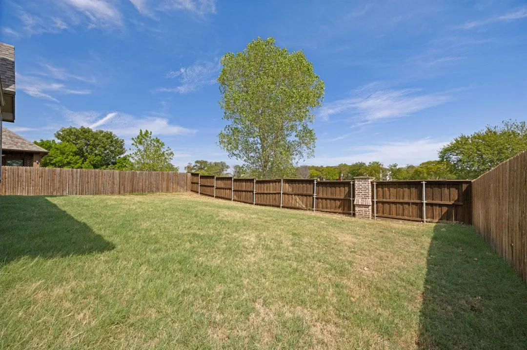 Expansive grassy yard with wood panel fencing and a brick column accent
