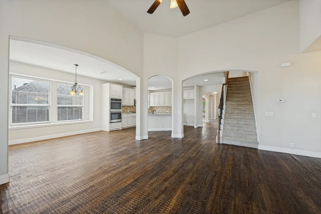 Vaulted ceiling, wood-finish flooring, arched doorways, built-in double ovens, and white cabinetry