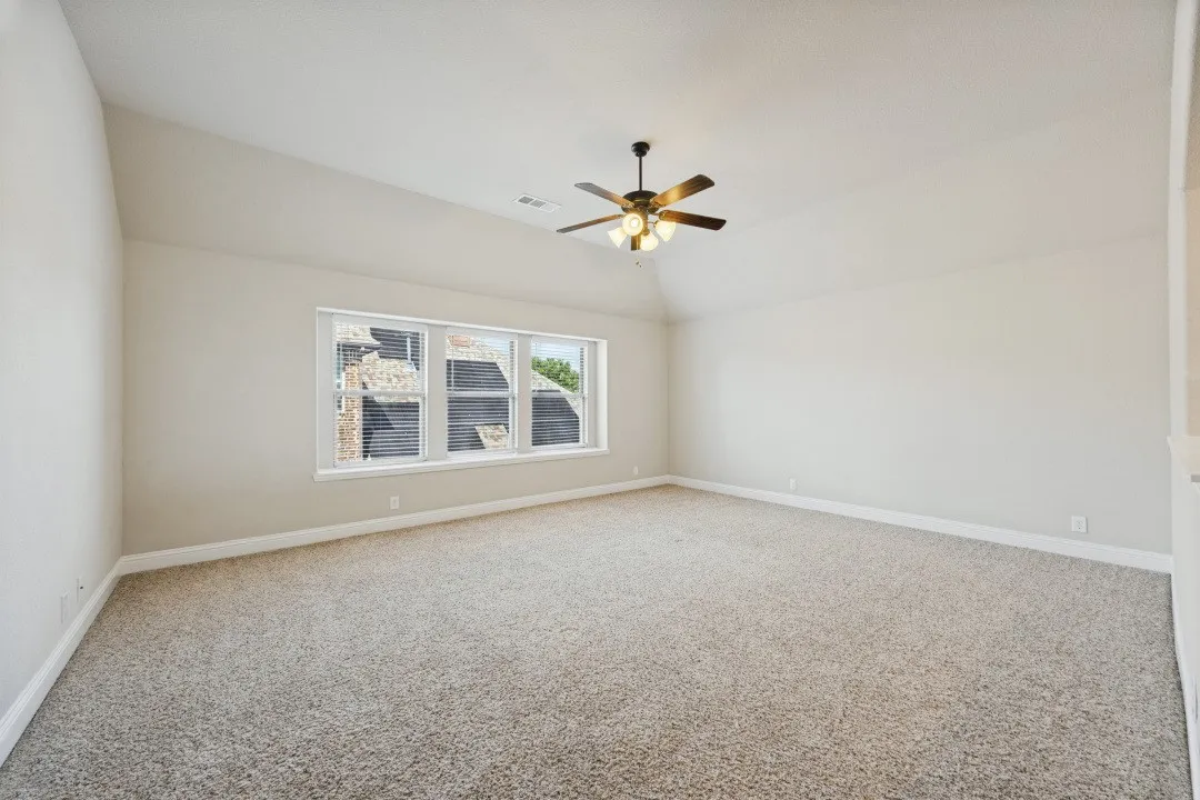 Spacious room featuring vaulted ceilings, light neutral carpeting, a multi-pane window with louvered shutters, and a ceiling fan with integrated lighting