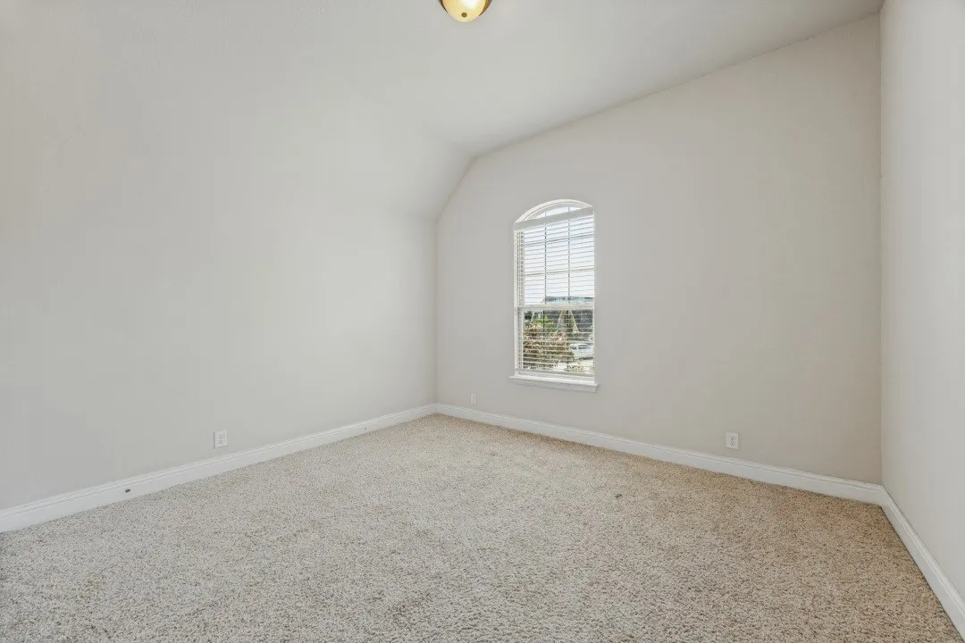 Carpeted room featuring a single arched window with blinds, a vaulted ceiling, and neutral-toned walls