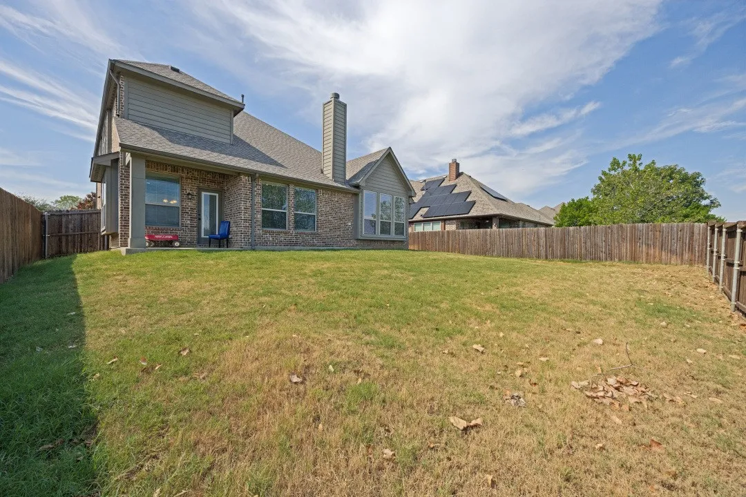 Expansive fenced backyard with a brick and siding exterior and a covered patio