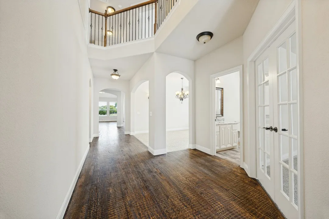 Rich wood-finish flooring, a two-story foyer, arched doorways, white French doors, and decorative iron balusters
