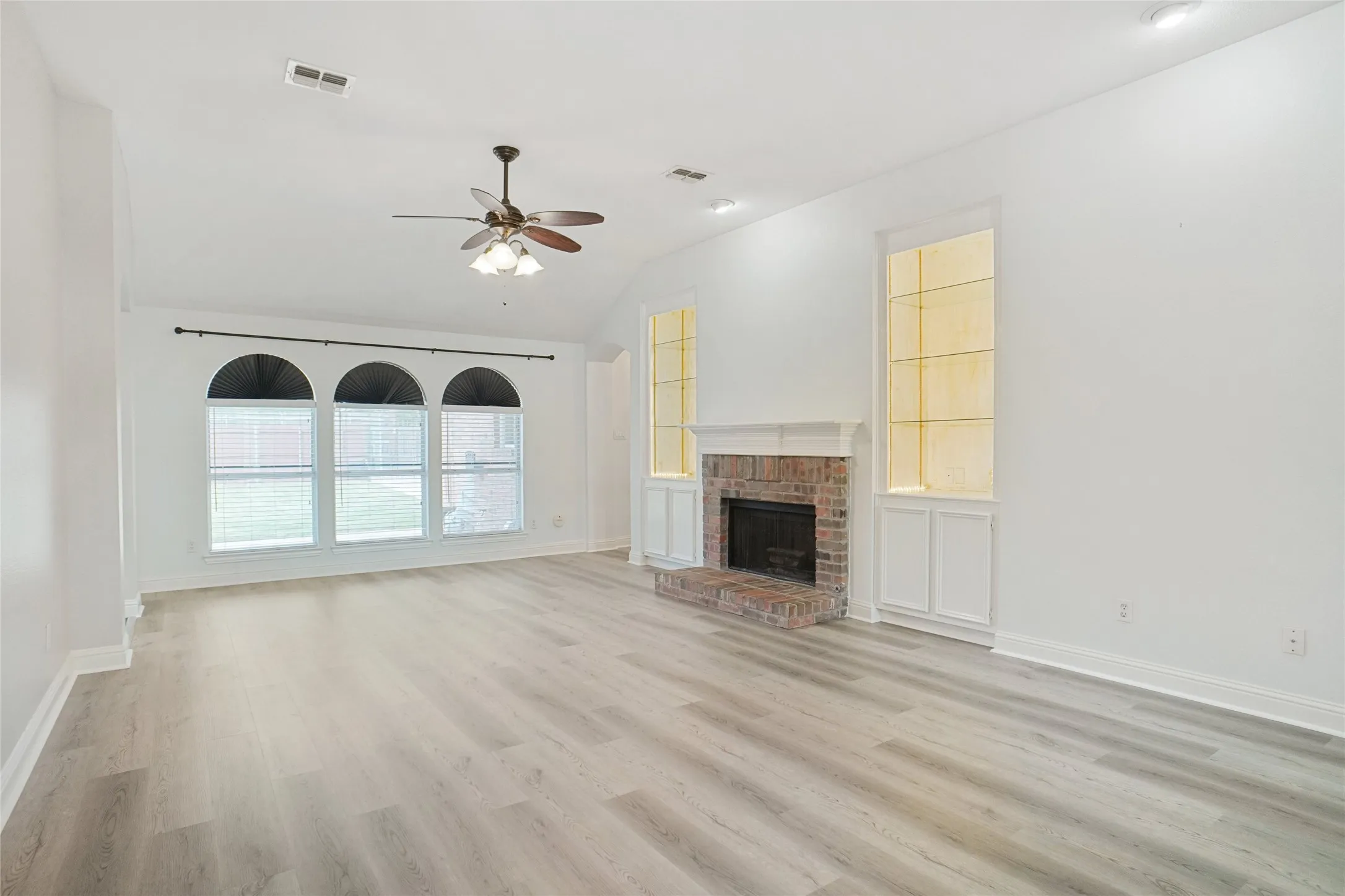 Unfurnished living room featuring a fireplace, light wood-style floors, ceiling fan, vaulted ceiling, and built in features