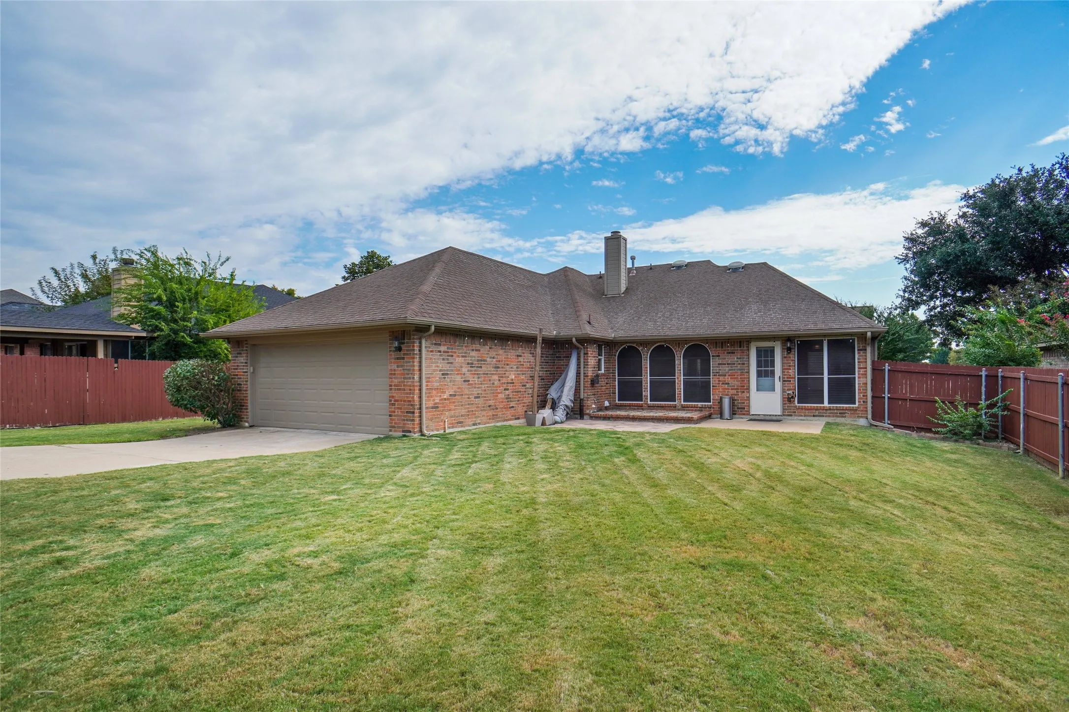 Ranch-style home with brick siding, a patio, concrete driveway, a shingled roof, and a garage