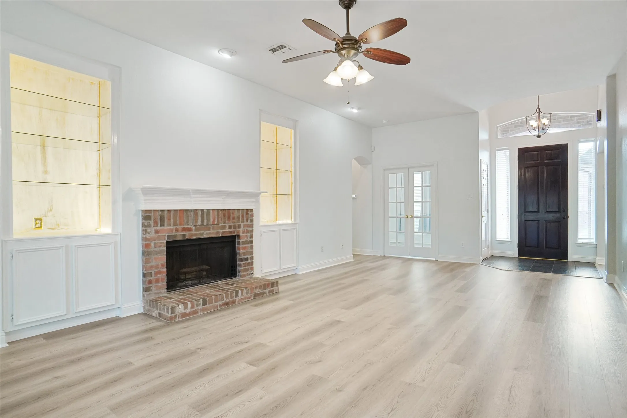 Unfurnished living room featuring a fireplace, light wood finished floors, french doors, and a ceiling fan