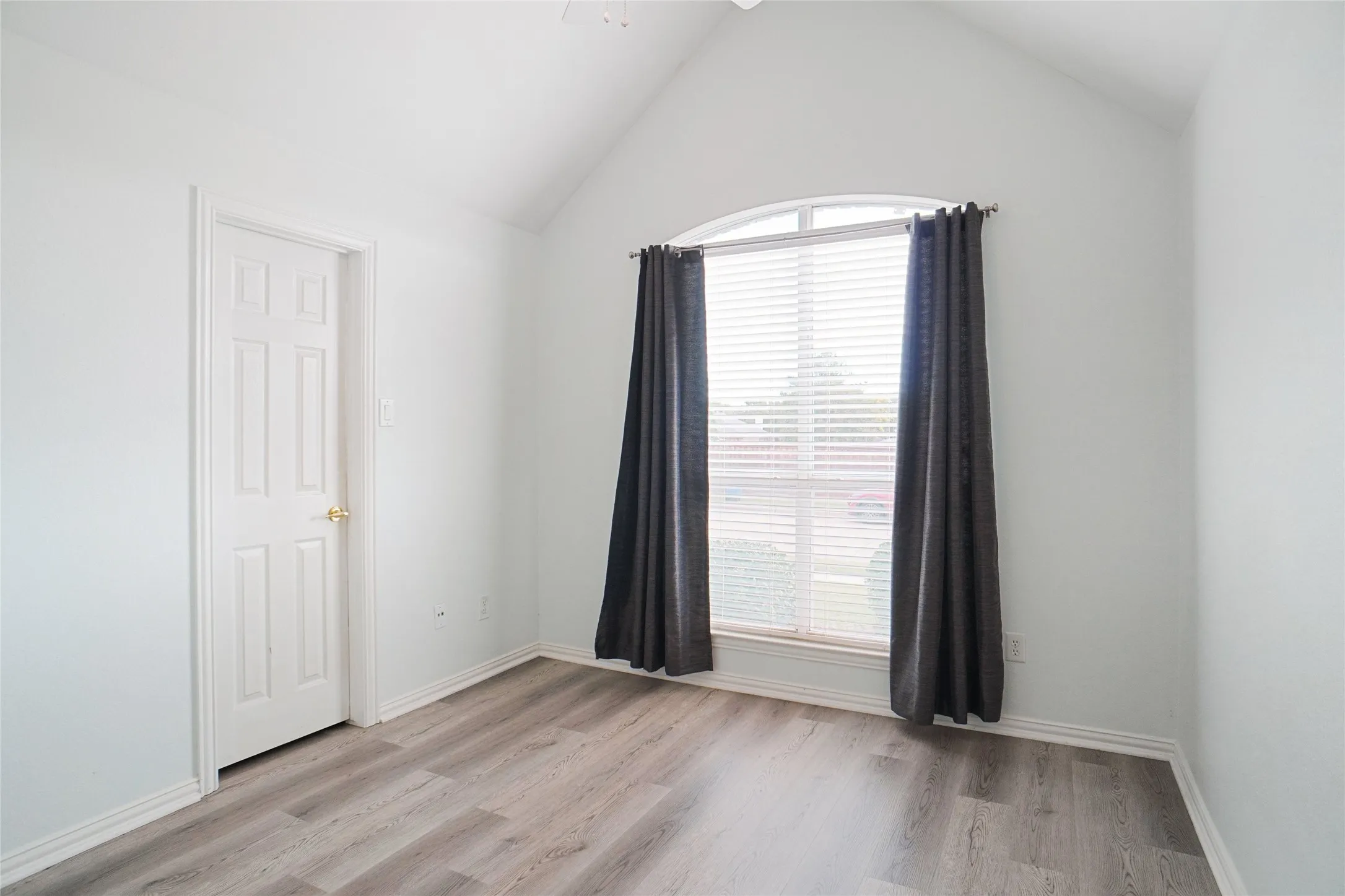 Empty room featuring light wood-style flooring, lofted ceiling, and ceiling fan