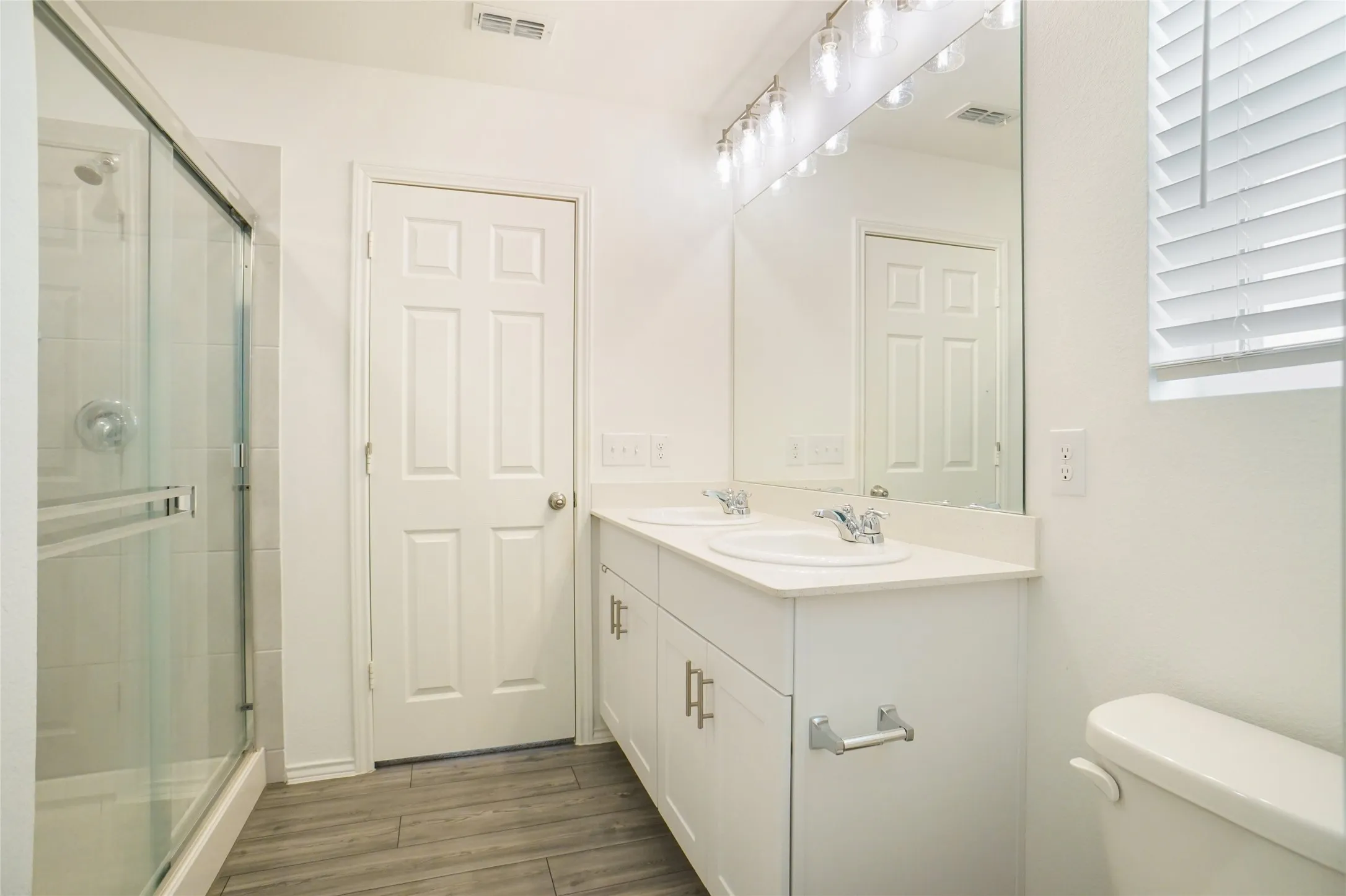 Full bath with double vanity, a shower stall, and light wood-style floors