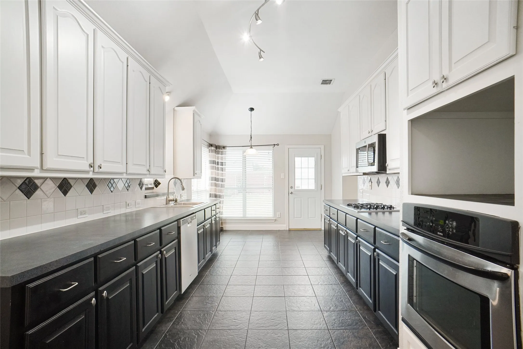 Kitchen featuring dark cabinetry, backsplash, white cabinets, stainless steel appliances, and pendant lighting
