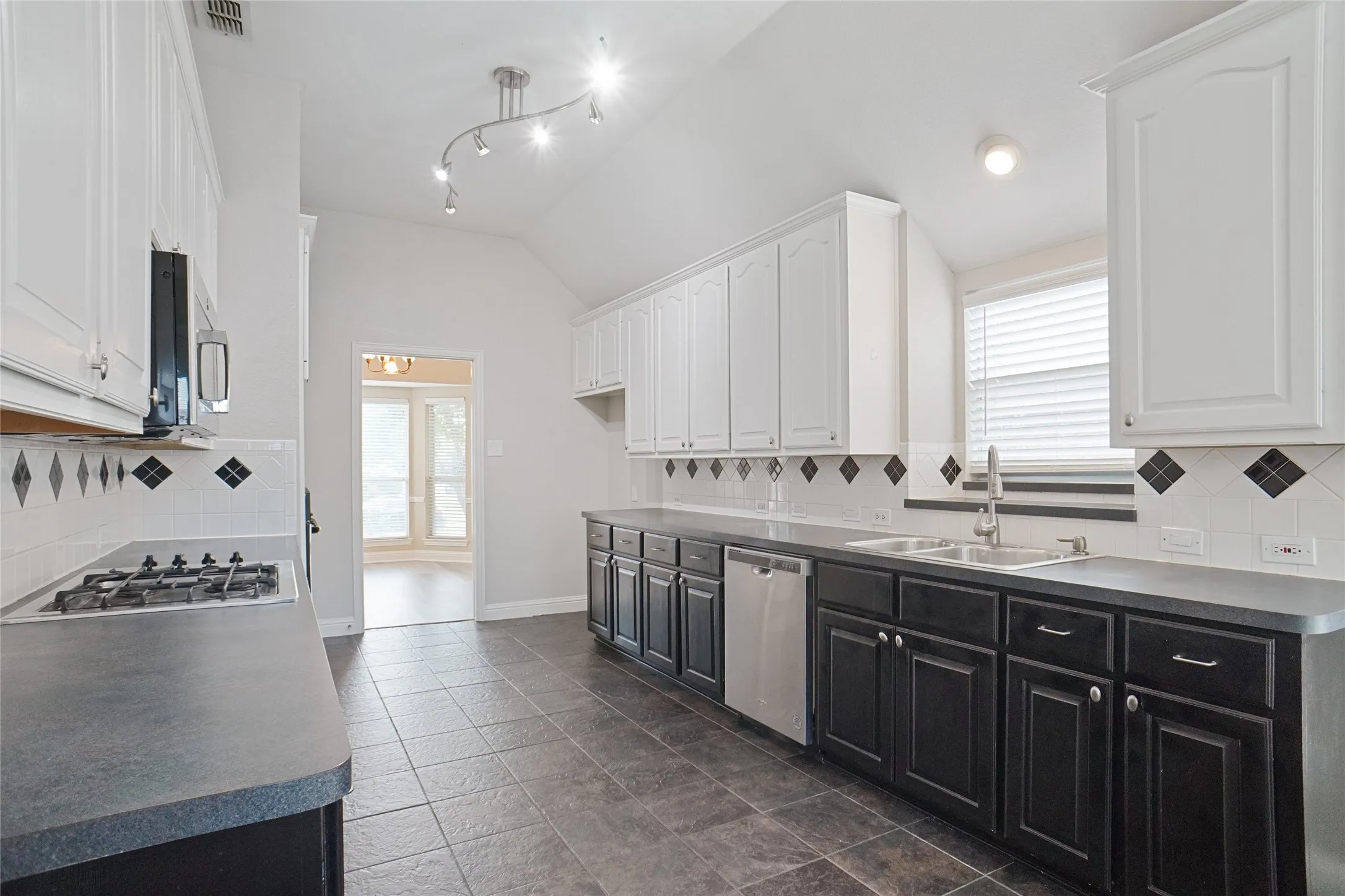 Kitchen featuring tasteful backsplash, dark cabinets, white cabinets, and lofted ceiling