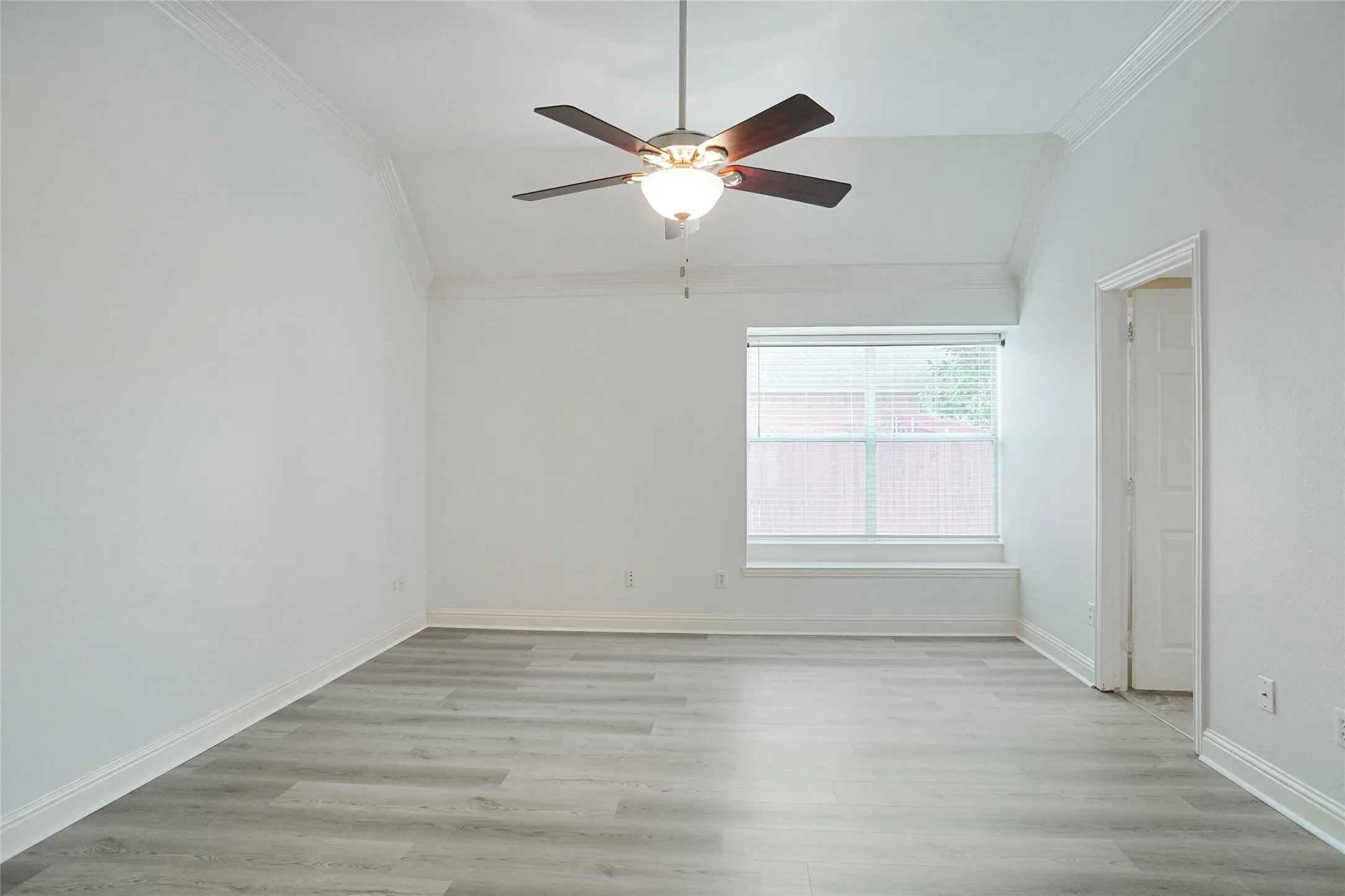 Empty room featuring crown molding, lofted ceiling, light wood-style floors, and a ceiling fan