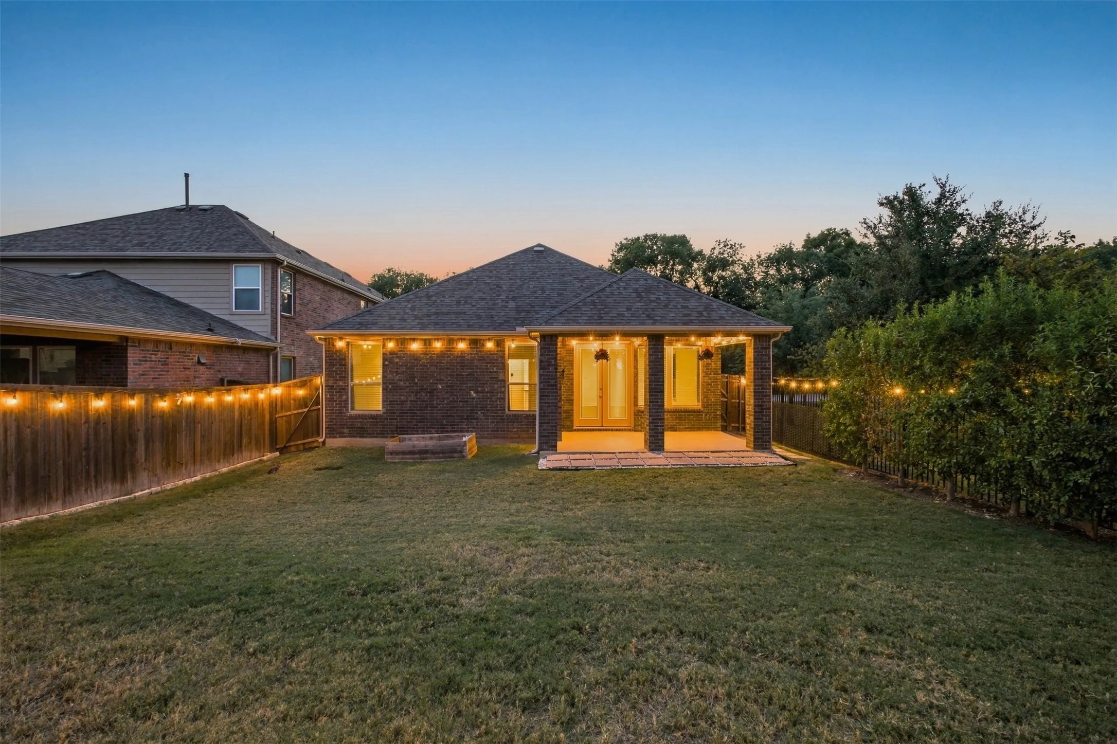 Expansive backyard featuring a manicured lawn, wood fencing, and a covered patio with brick columns