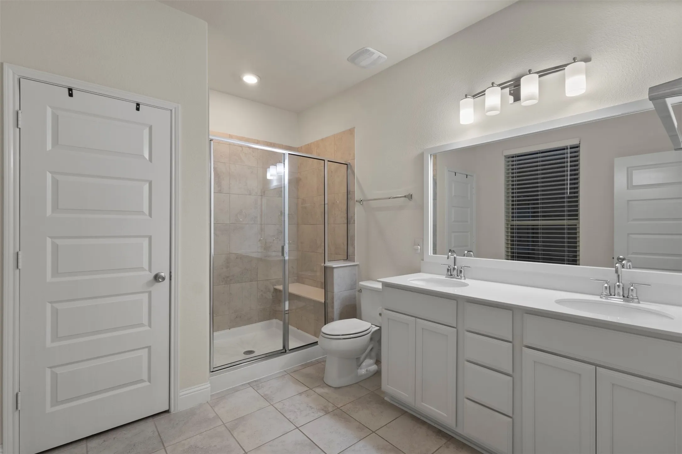 Dual vanity with white cabinetry, a large frameless mirror, and overhead lighting
