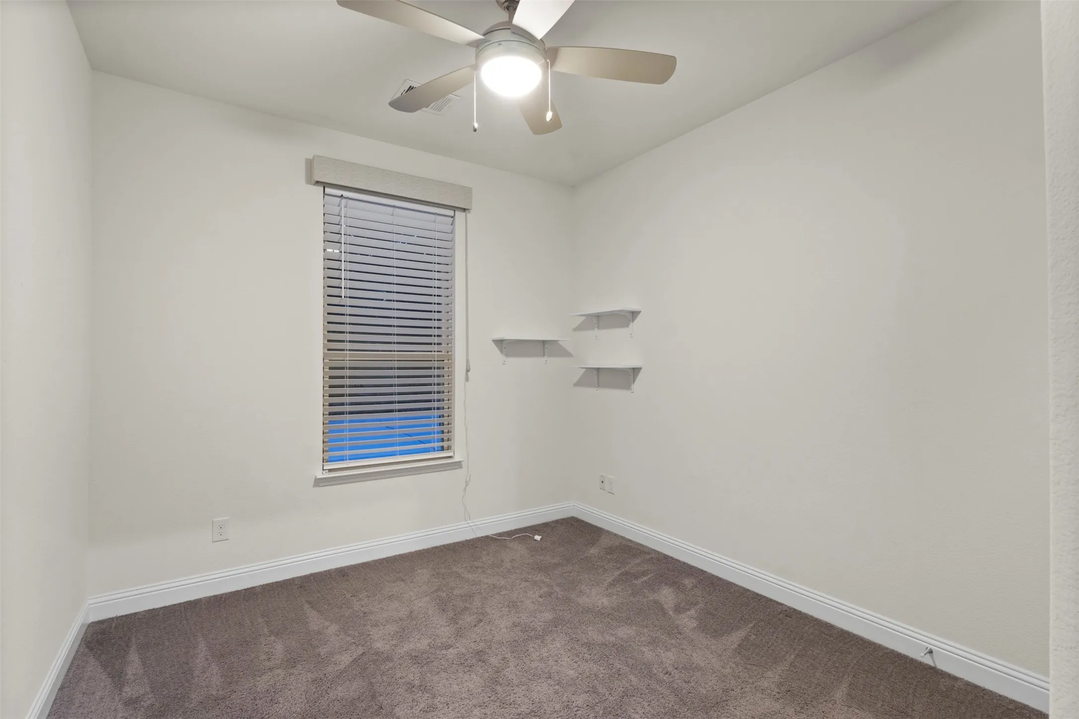 Neutral wall tones with a ceiling fan, window with blinds, and two wall-mounted floating shelves