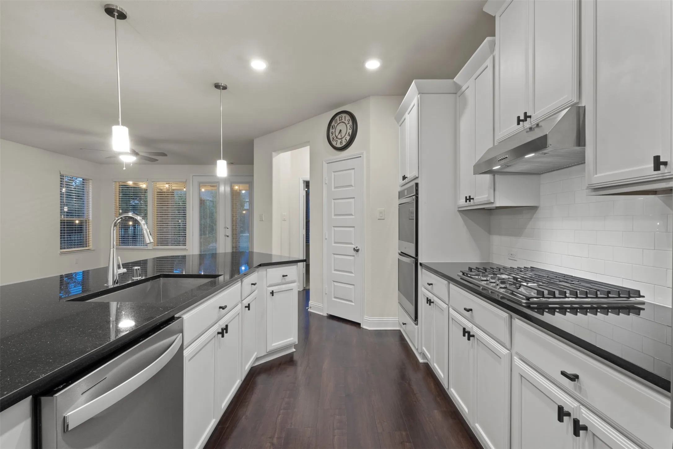White cabinetry with dark hardware, dark stone countertops, stainless steel appliances, and wood-finish flooring