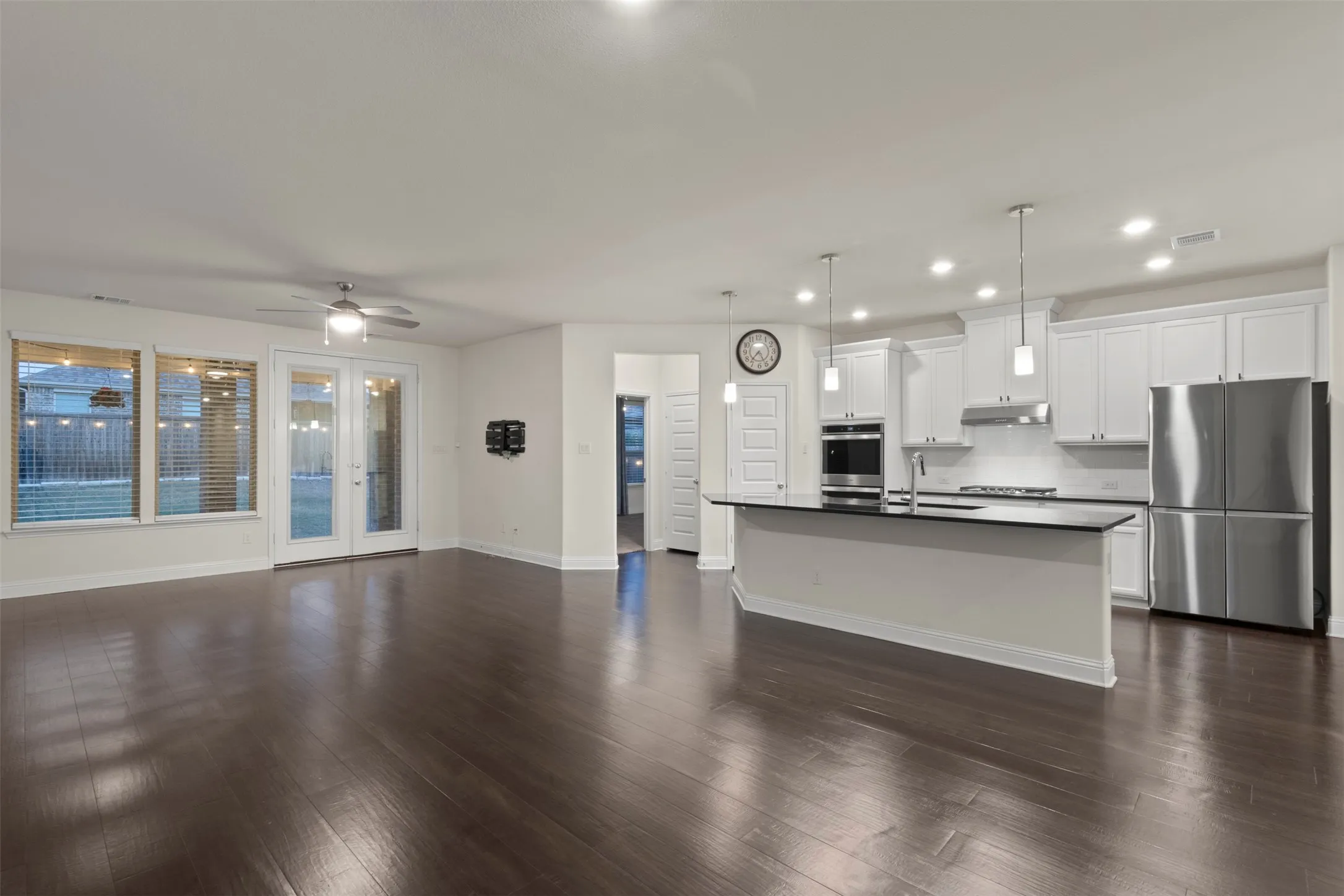 Hardwood-finish flooring, white cabinetry, stainless steel appliances, kitchen island with dark countertop, and recessed lighting