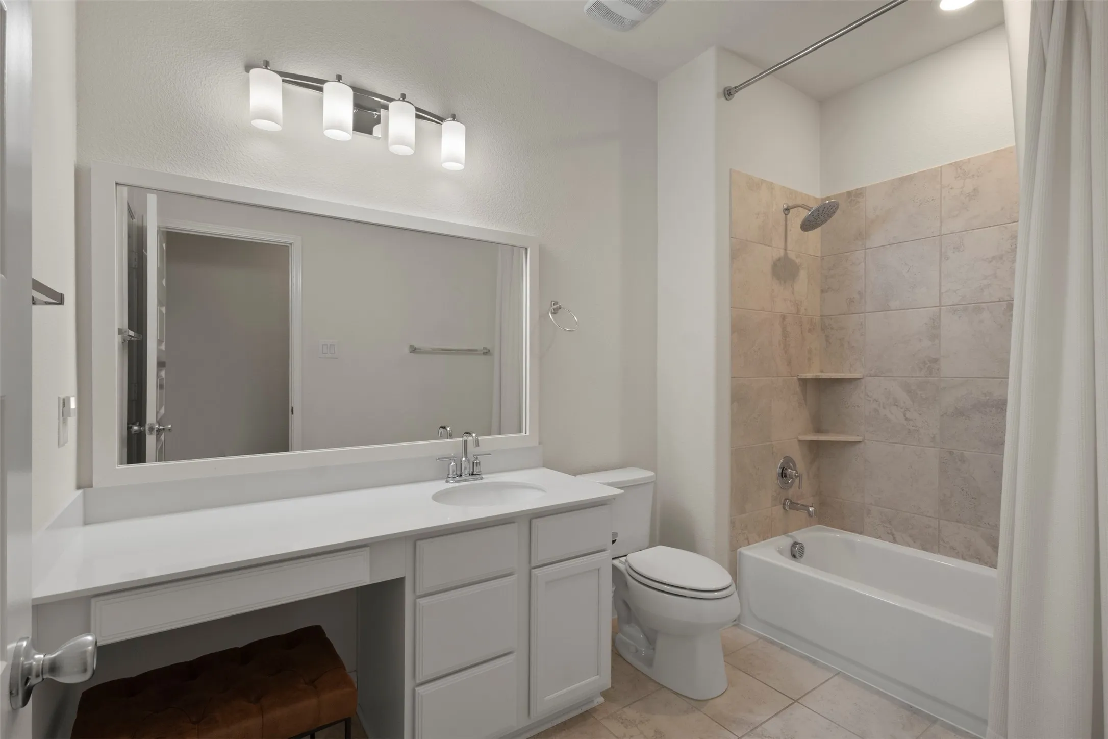 White vanity with integrated sink, expansive framed mirror, contemporary four-light fixture, tub with tiled surround, and built-in shower shelving