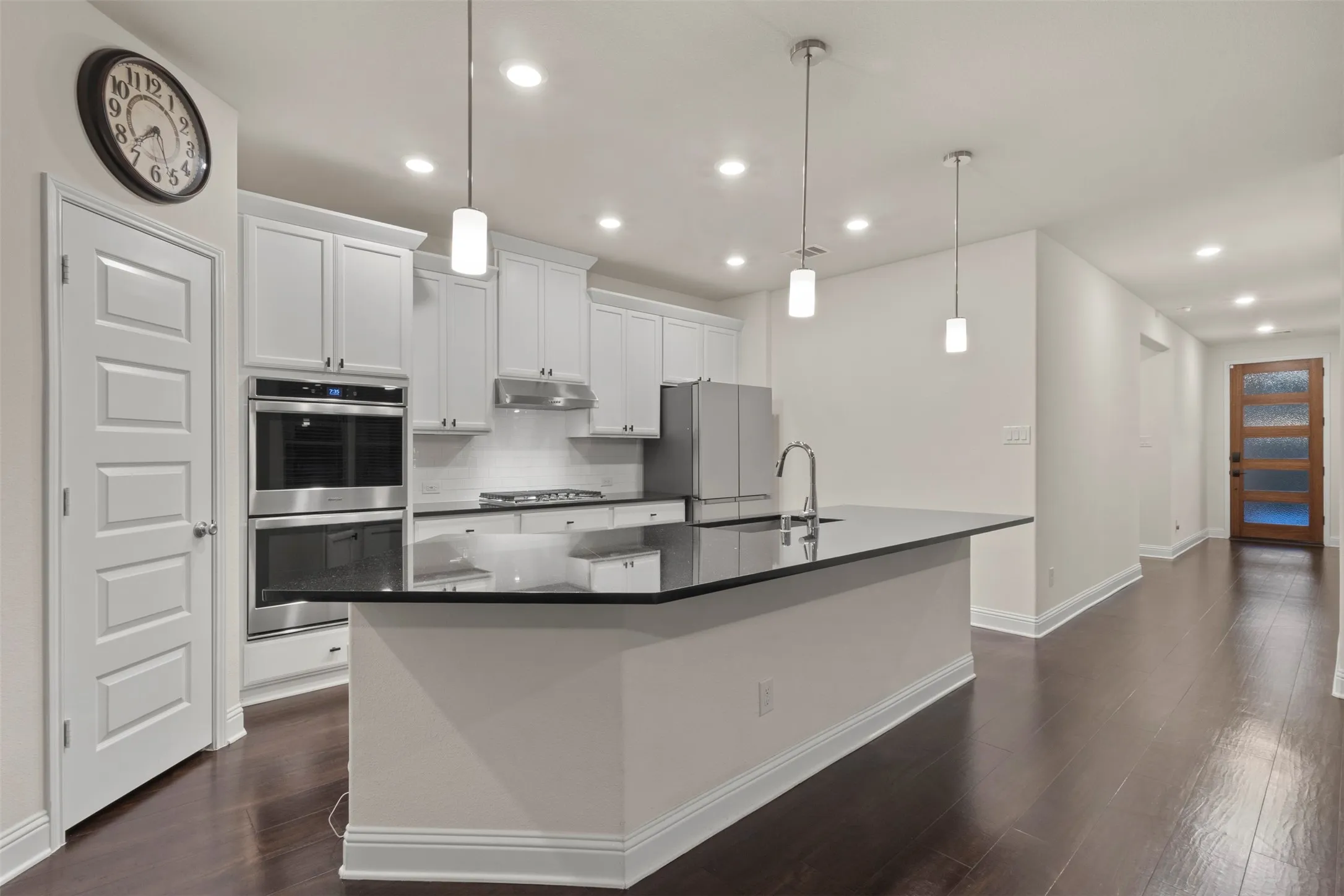 Open-concept kitchen with a large island, white shaker cabinetry, stainless steel appliances, and dark wood-finish flooring