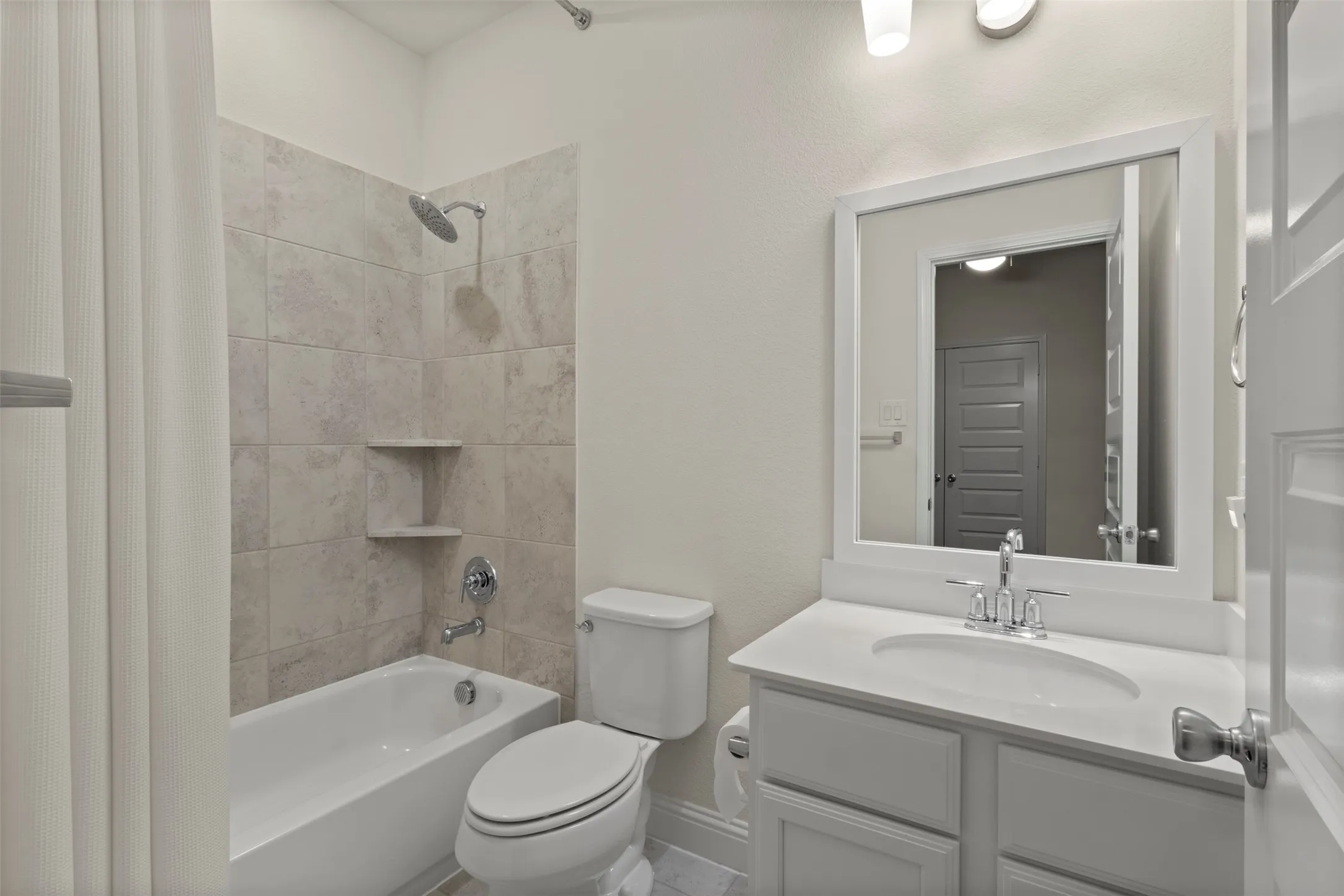 Full bathroom featuring a white vanity with an integrated sink, a framed mirror, and a tub with tiled surround and built-in shelving
