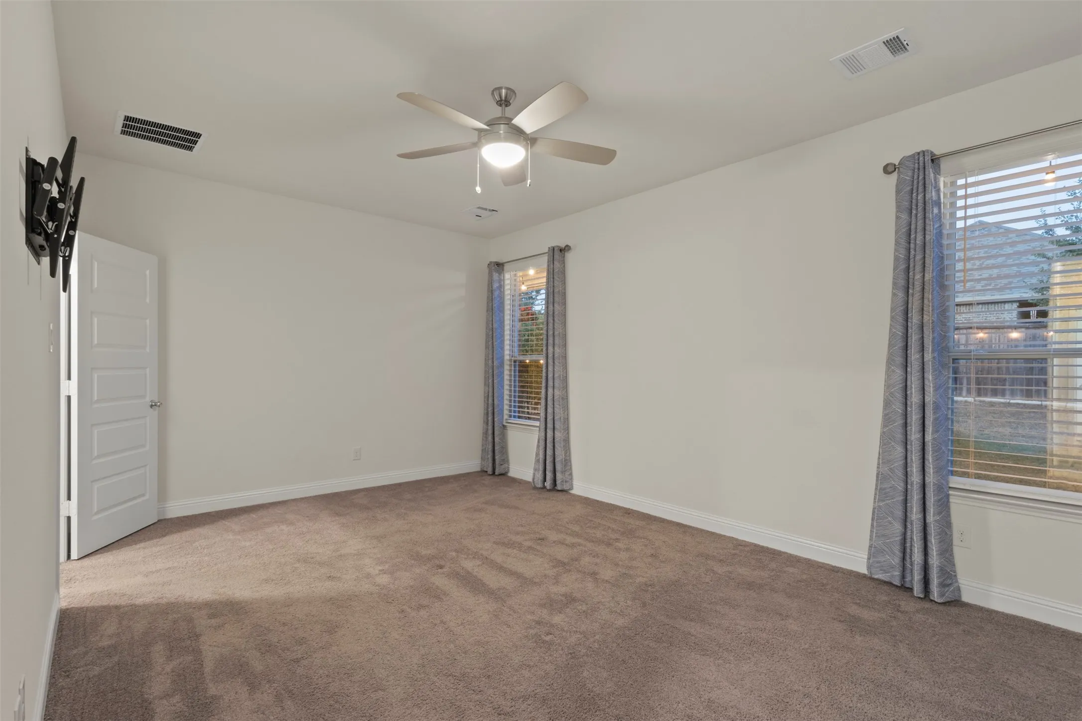 Neutral tone walls, plush carpet flooring, two windows with blinds, ceiling fan with integrated lighting, and a white paneled door