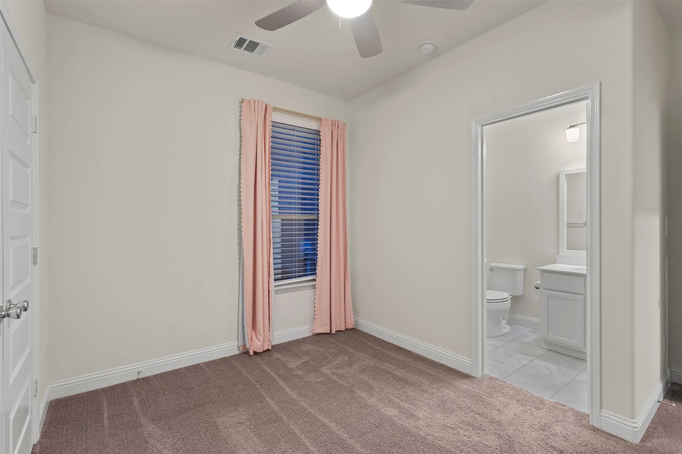 Neutral carpet flooring, overhead ceiling fan, and a window with blinds