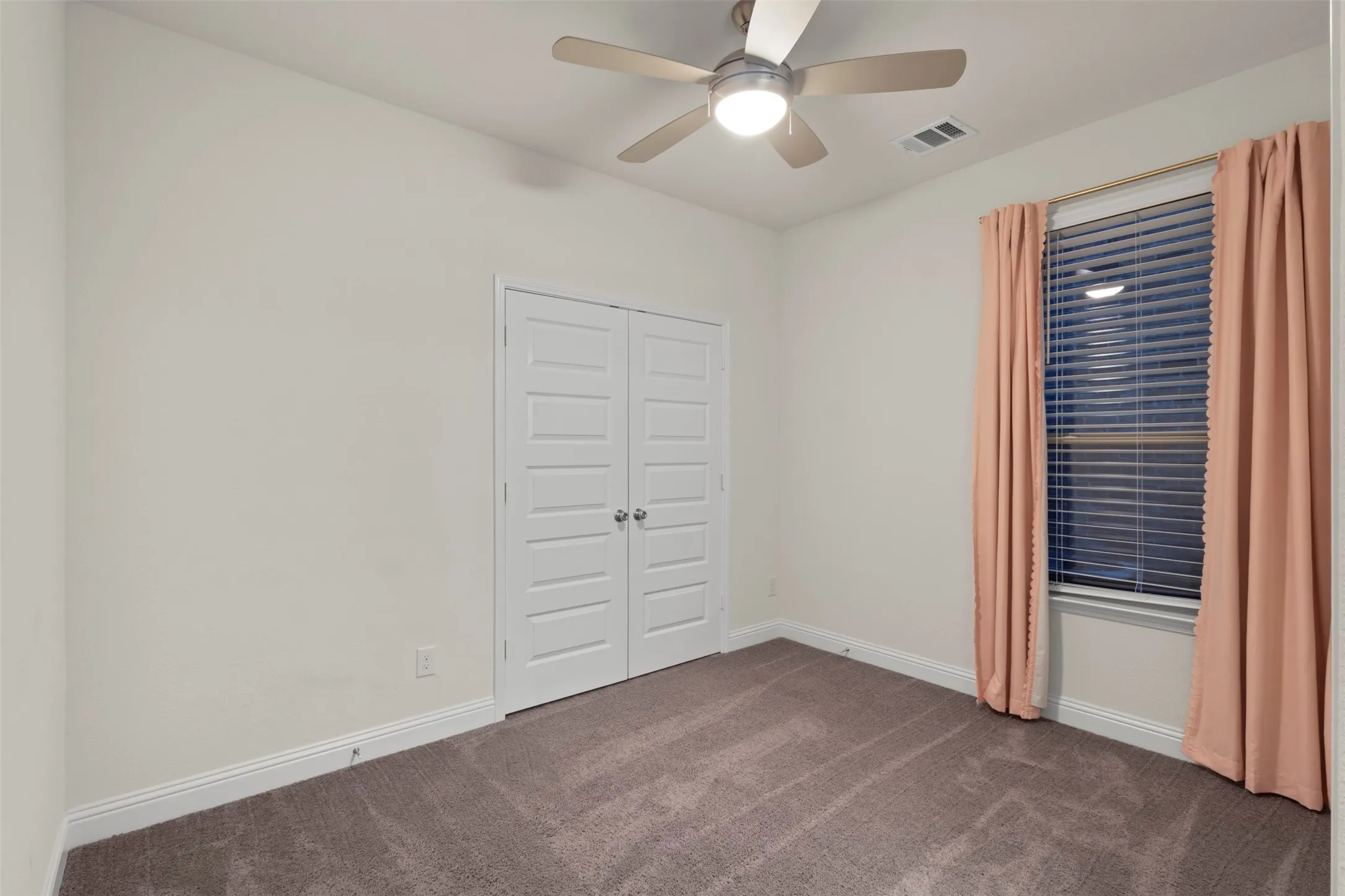 Neutral wall finishes, textured carpeting, double panel doors, and a ceiling fan with integrated lighting