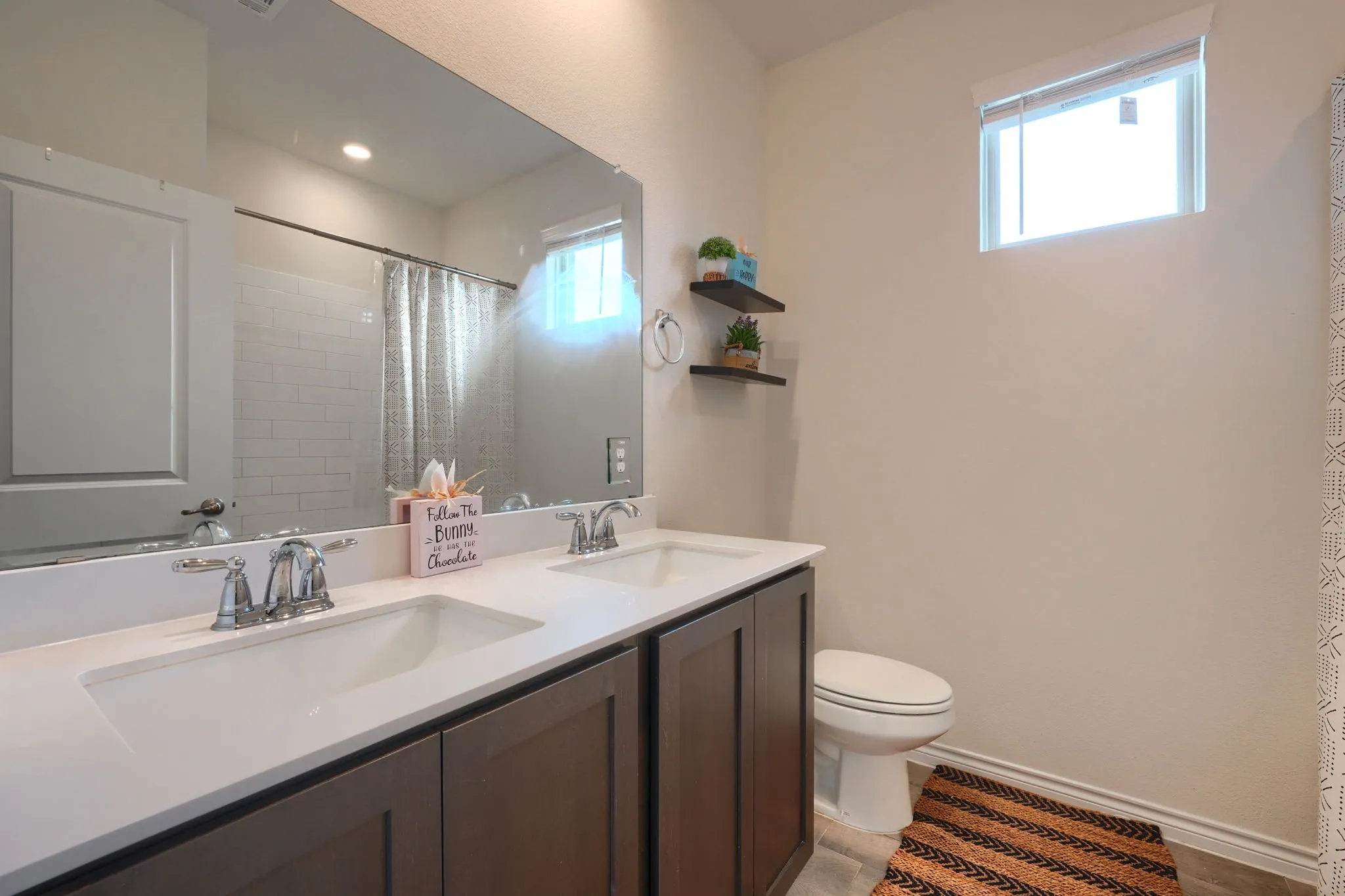 Dual-vanity bathroom featuring a white quartz countertop, dark wood cabinetry with ample storage, chrome faucet fixtures, and a large framed mirror