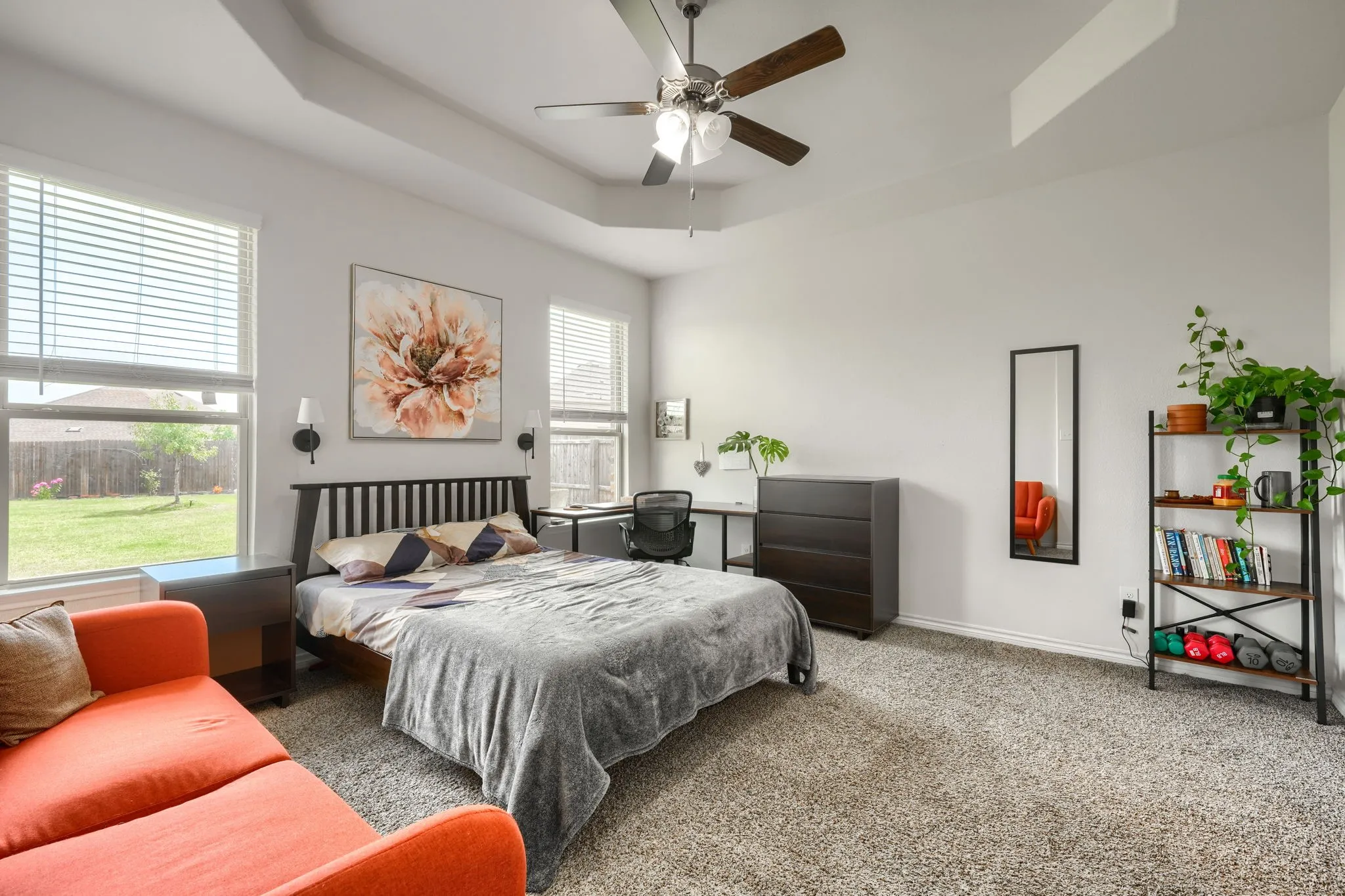 Tray ceiling with a ceiling fan, dual windows with blinds, and carpeted flooring
