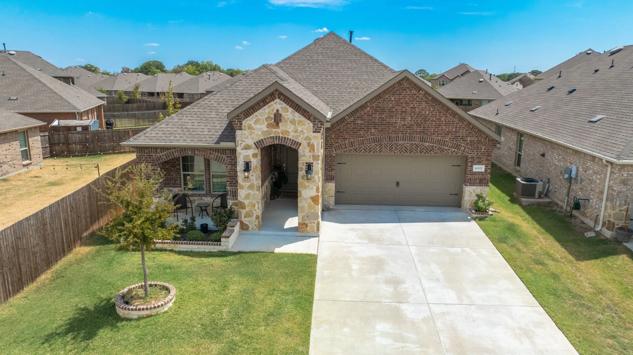 Brick and stone exterior featuring an arched entry, covered front porch, attached garage, and concrete driveway