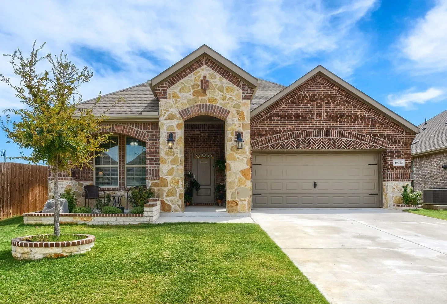 Brick and stone exterior with an arched entry, attached garage, concrete driveway, and front landscaping