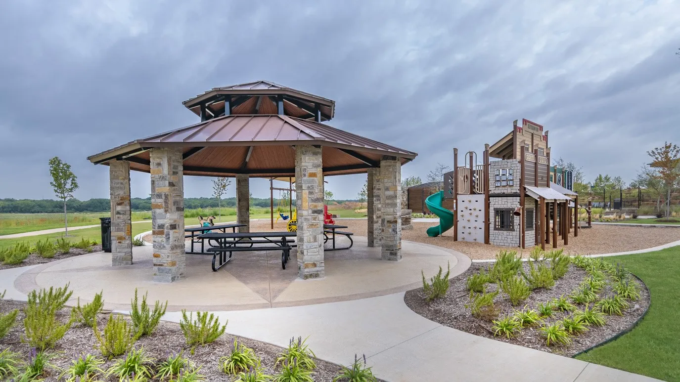 Stone-columned gazebo with a metal roof, concrete patio, and built-in picnic tables