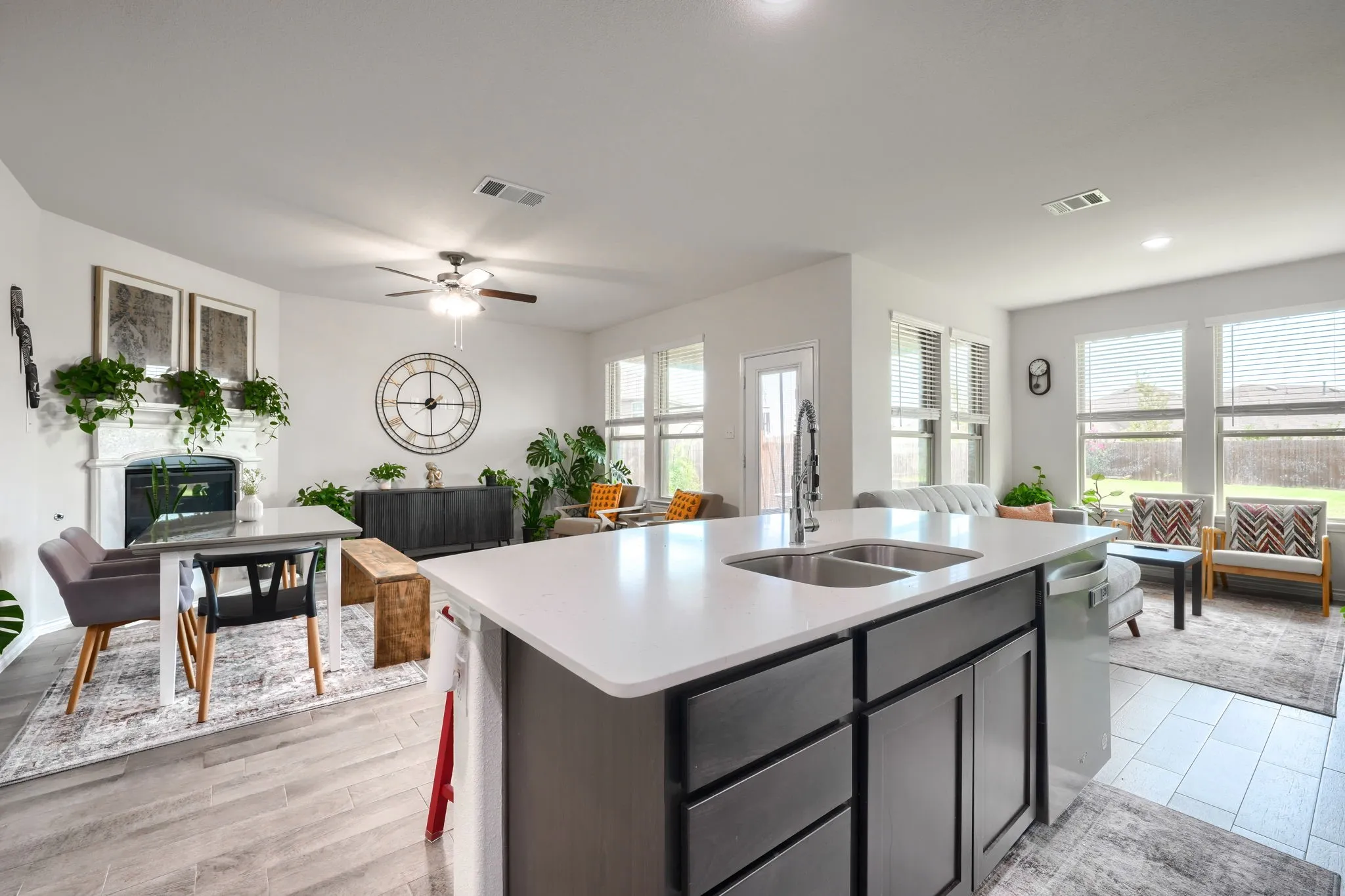 Kitchen island with a double basin sink and a high-arc faucet, adjacent to a living area with large windows and a fireplace