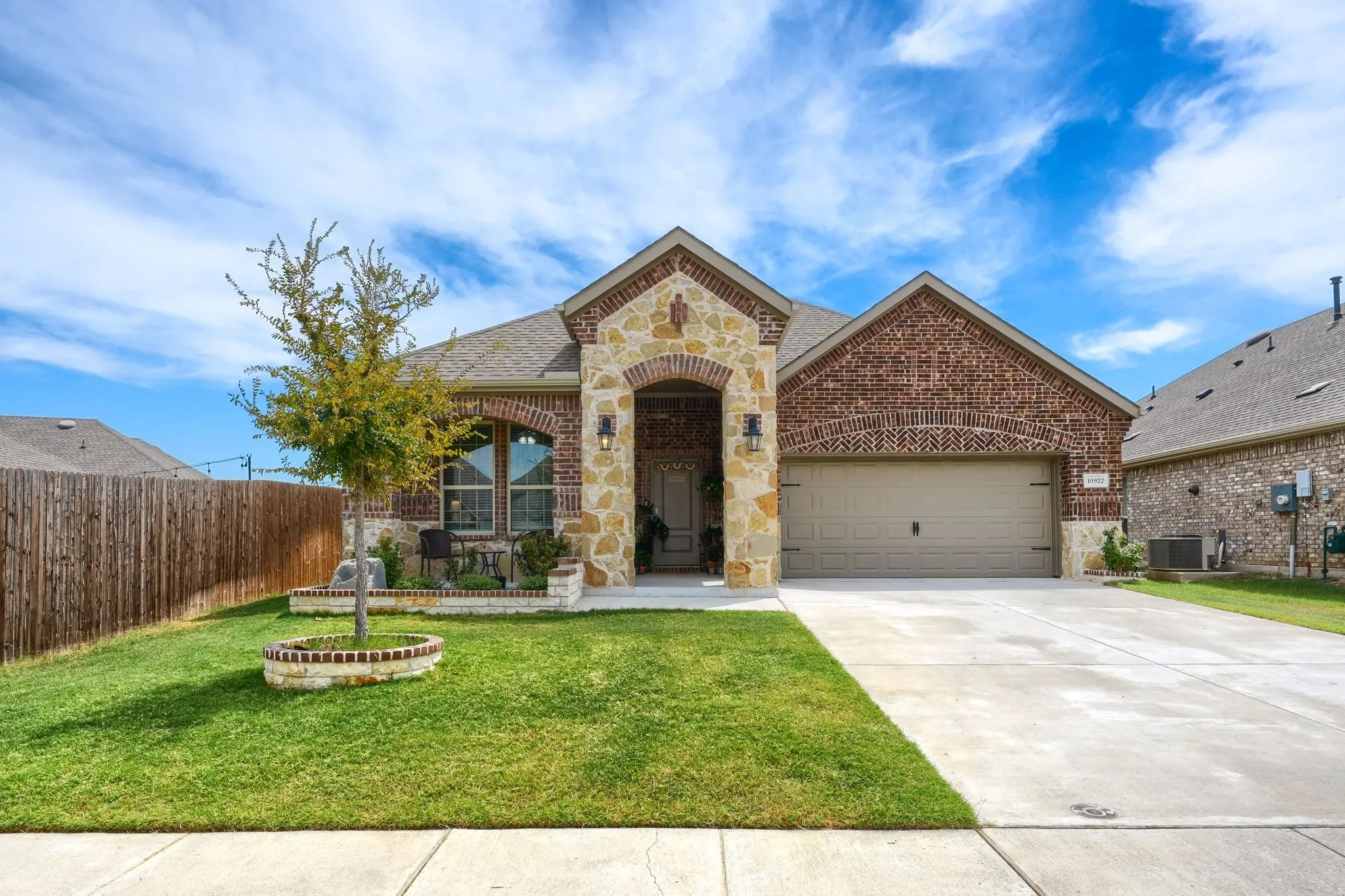 Charming brick and stone residence showcasing an arched entryway with decorative stone detailing, two-car garage, and manicured front lawn with mature landscaping
