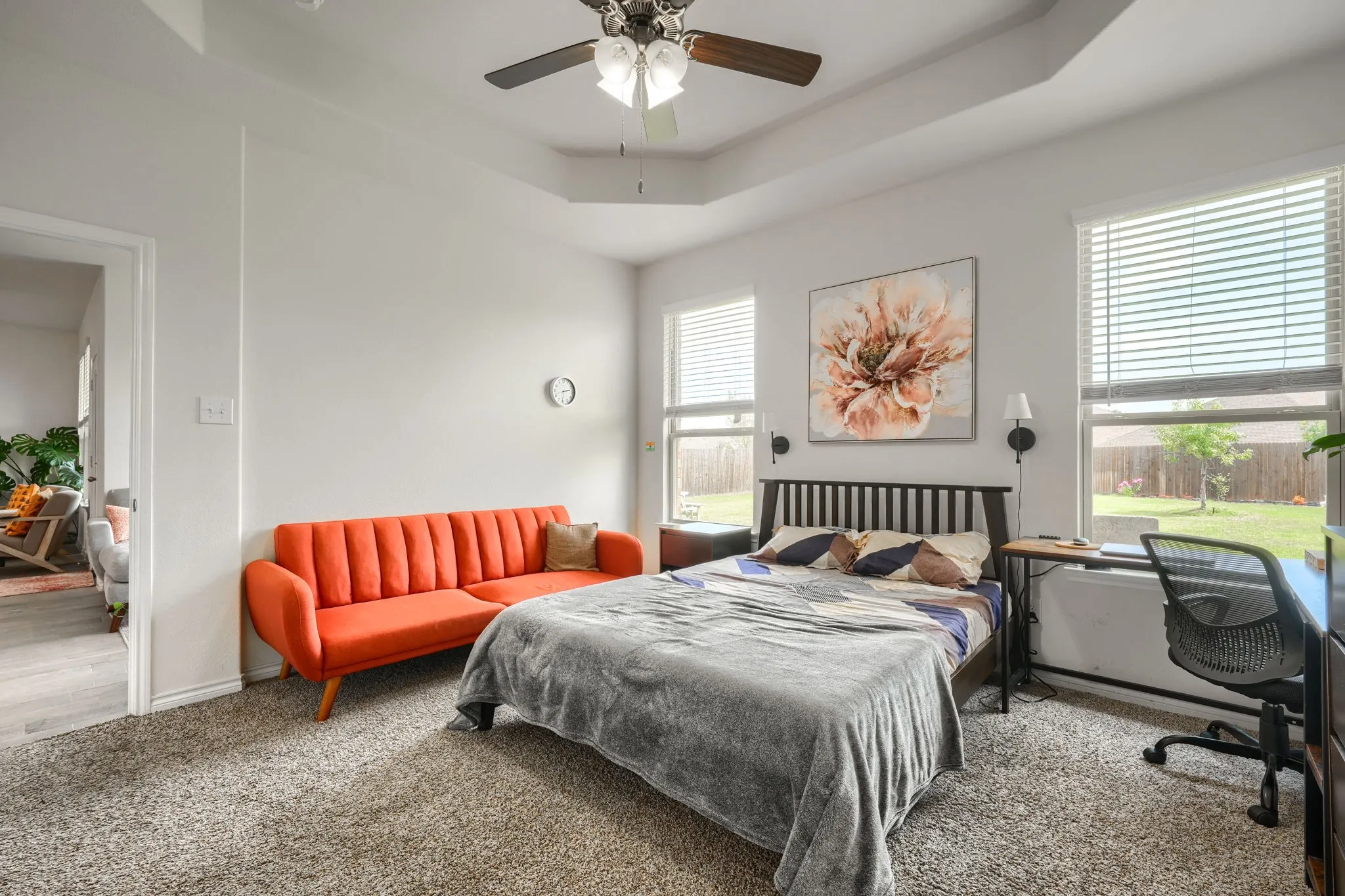 Recessed tray ceiling, neutral-toned carpeting, dual windows with blinds, and a ceiling fan with integrated lighting