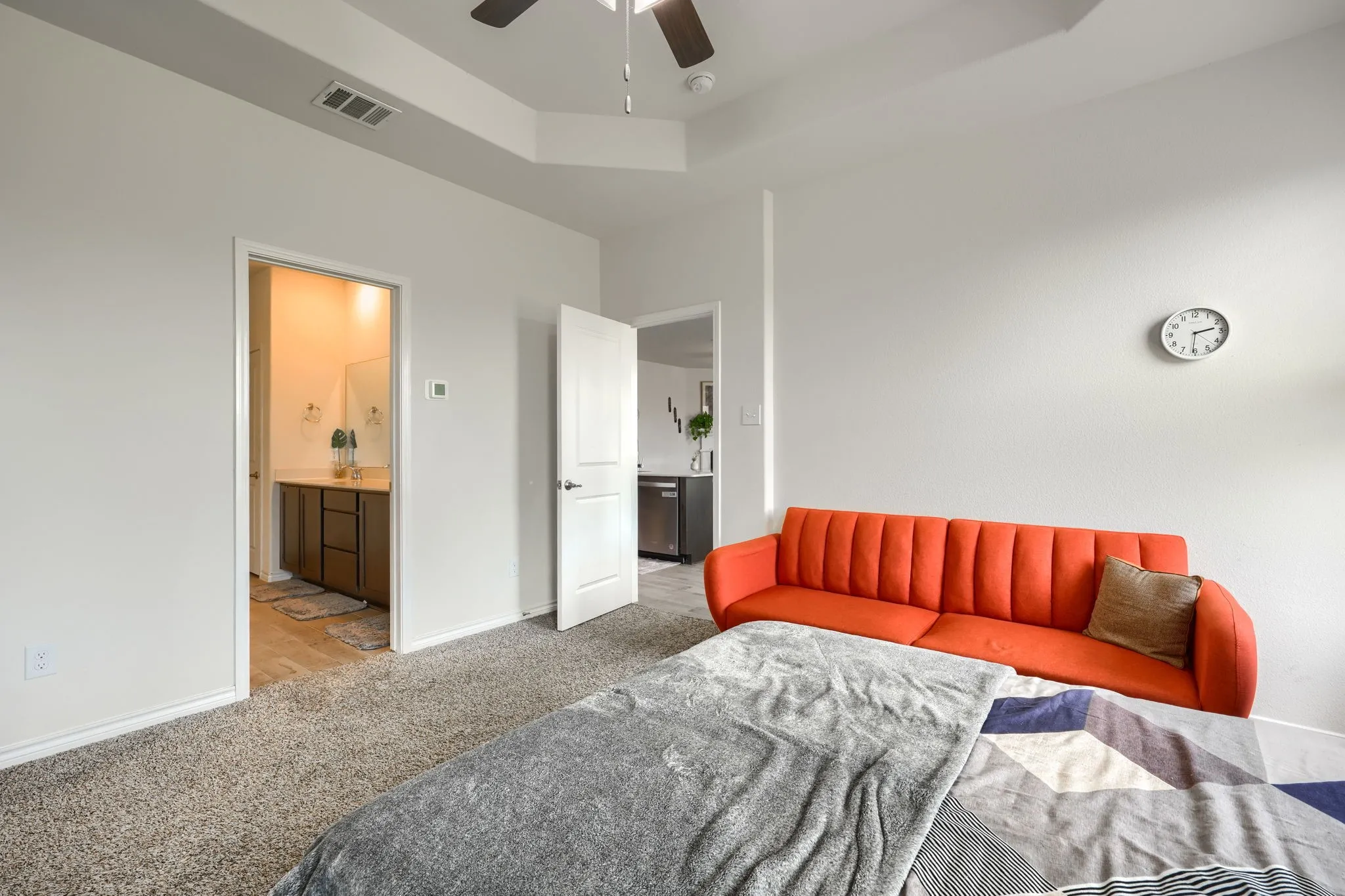 Tray ceiling with a ceiling fan, carpeted flooring, and a bathroom featuring a vanity with under-sink cabinetry