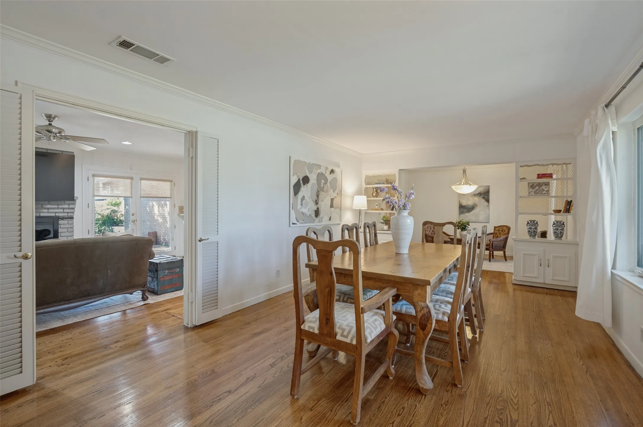 Hardwood flooring, crown molding, built-in shelving, white window trim, and louvered double doors