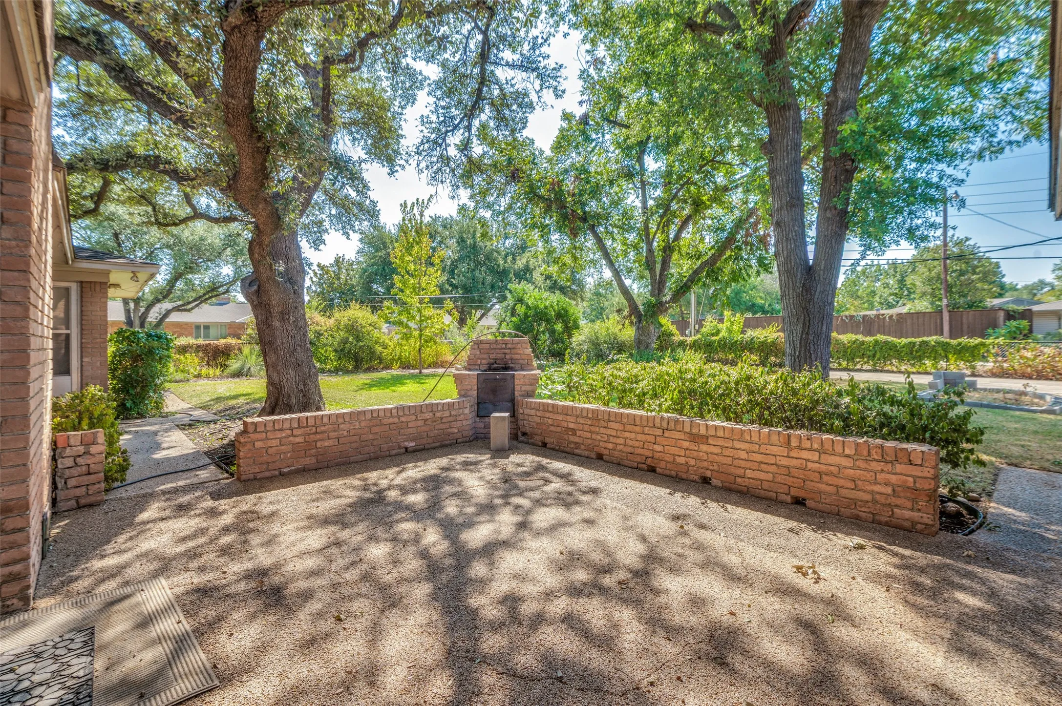 Brick patio featuring an integrated brick grill, mature trees, and a concrete pathway