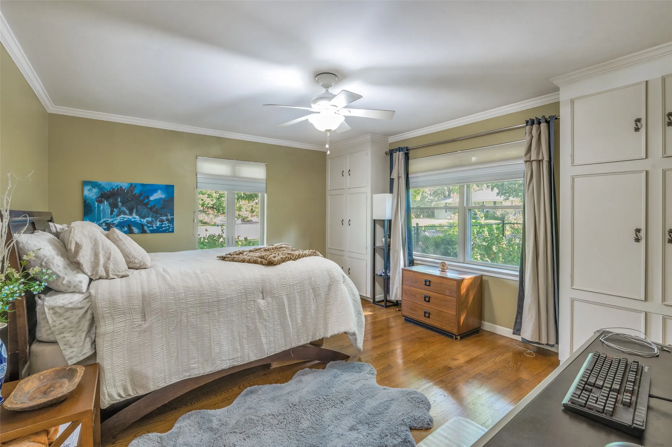 Built-in white cabinetry, ceiling fan, wood-finish flooring, and crown molding