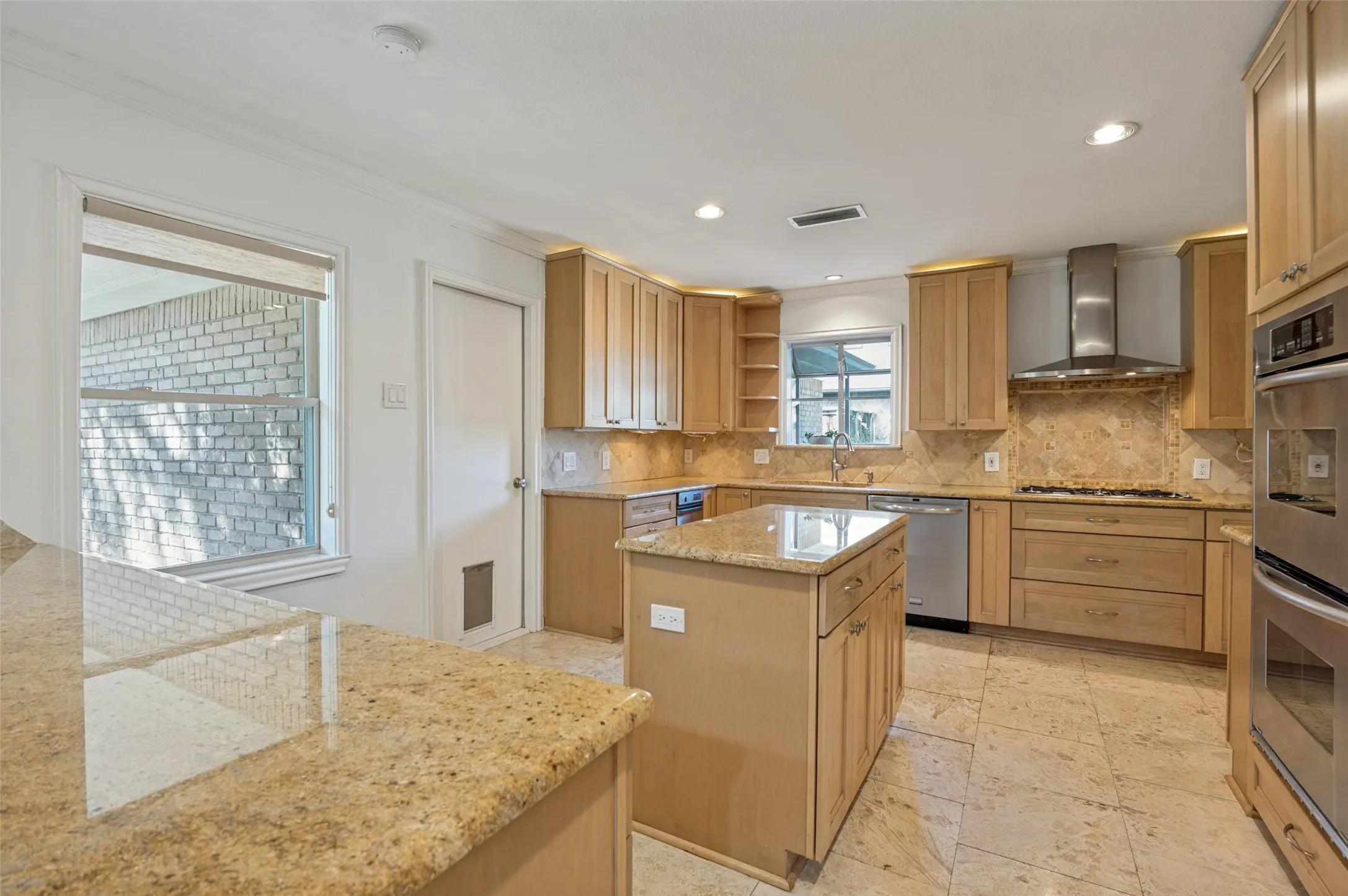 Kitchen featuring light wood cabinetry, stone countertops, stone tile flooring, a central island, and stainless steel appliances