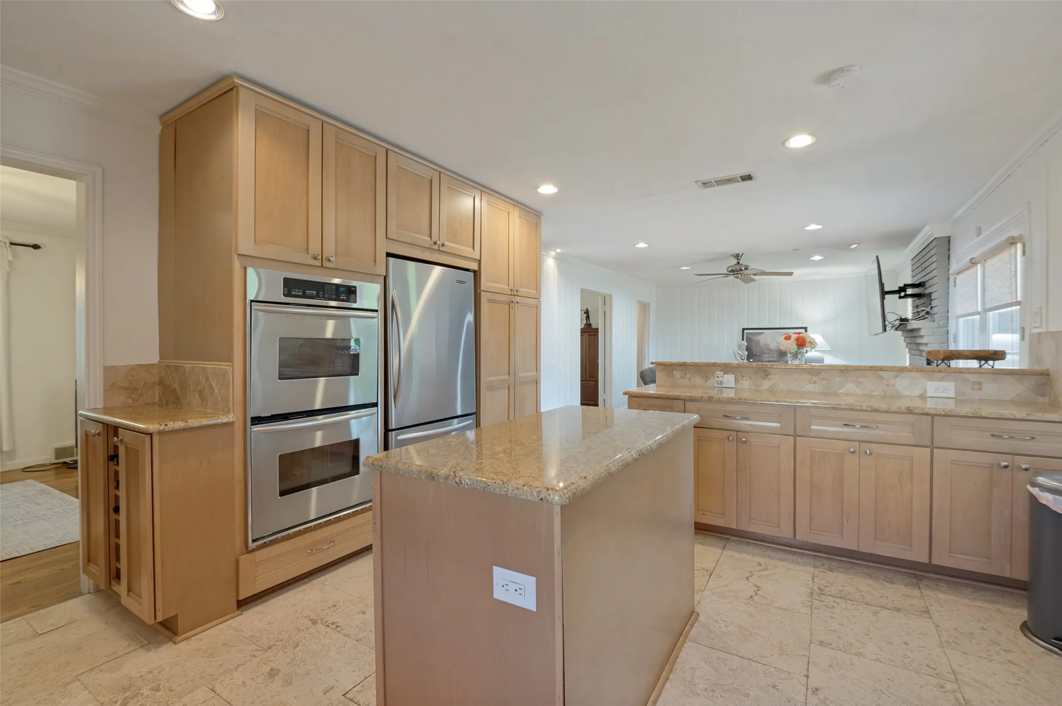 Kitchen with tiled flooring, light wood-finish cabinetry, stainless steel double ovens, and a center island with a granite countertop
