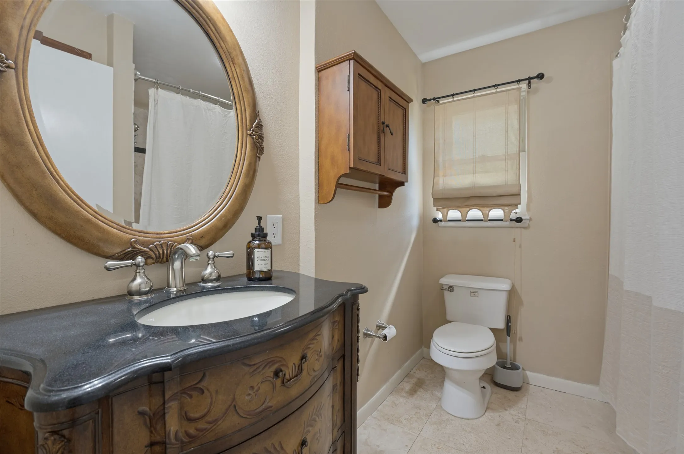 Vanity with a dark countertop and undermount sink, an ornamental framed mirror, and a wall-mounted wooden cabinet