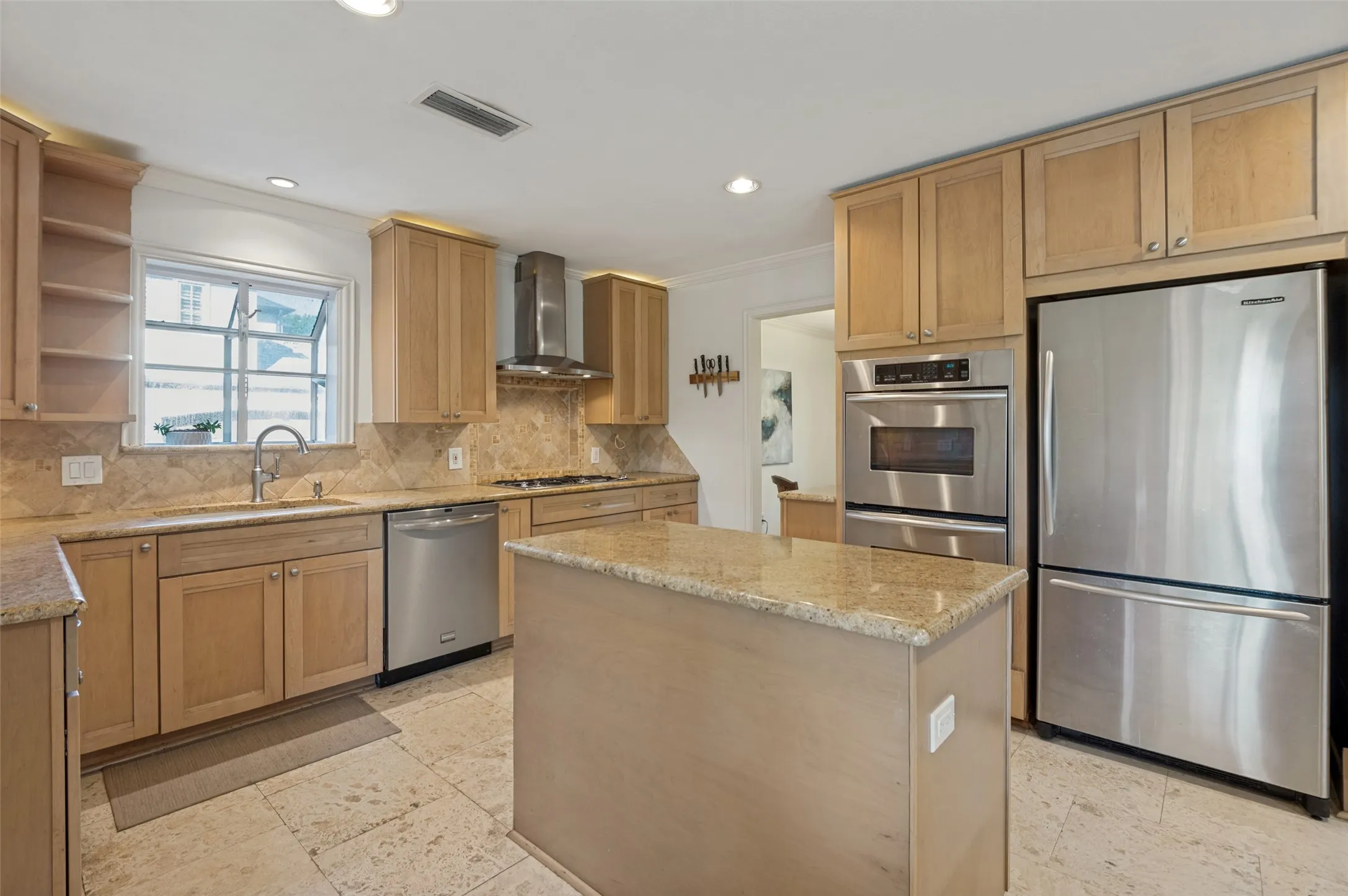 Kitchen featuring light wood cabinetry, stainless steel appliances, a center island with countertop, stone tile flooring, and recessed lighting