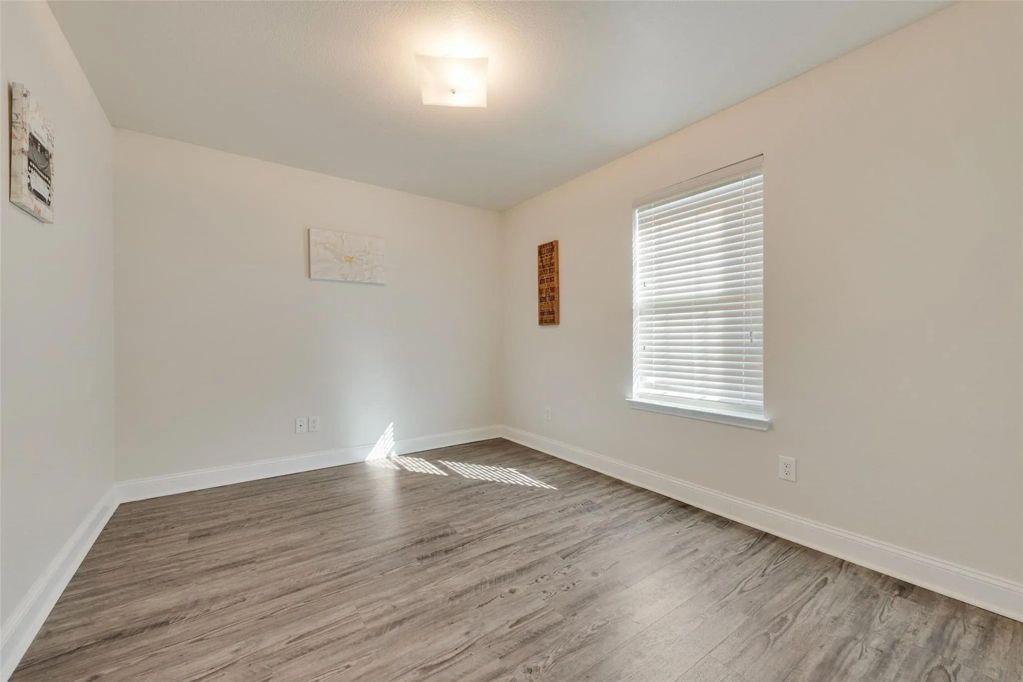 Recessed window with blinds, wood-finish flooring, white trim, and a ceiling-mounted light fixture