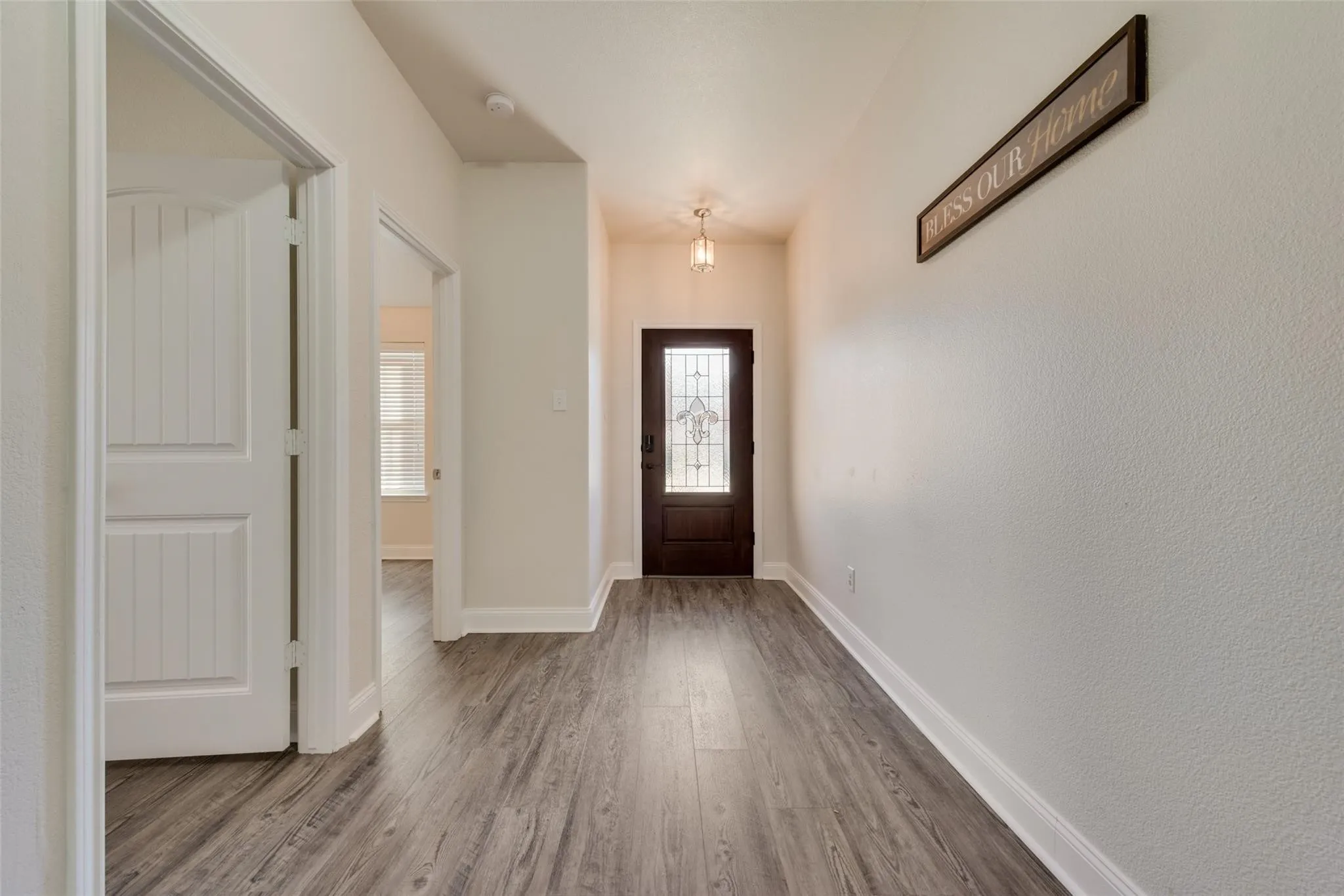 Wood-finish flooring throughout, white trim, and a dark-stained entry door with decorative glass