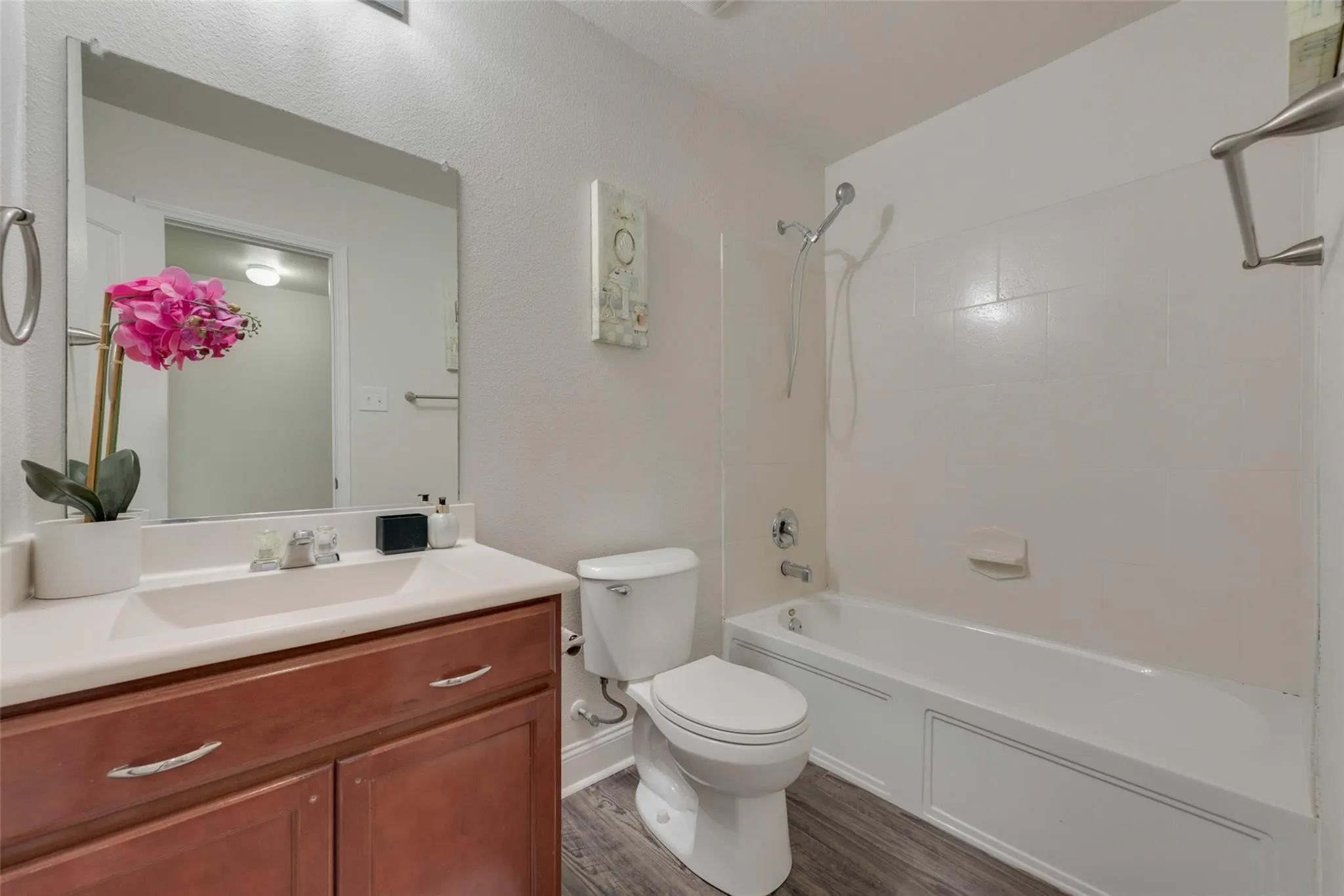 Wood-finish flooring, white vanity countertop, and dark wood-finish cabinetry with silver hardware