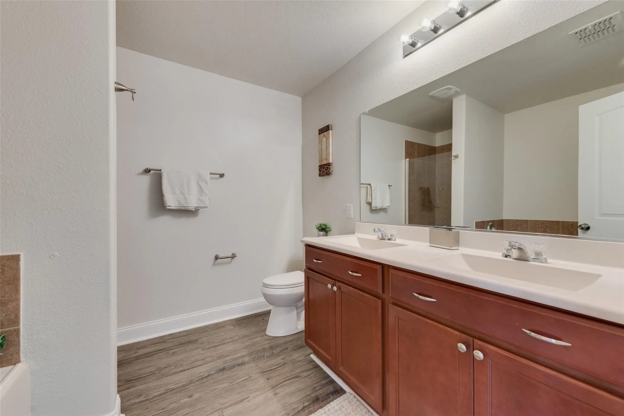 Dual vanity with integrated sinks, wood-finish cabinetry, and a large wall-mounted mirror
