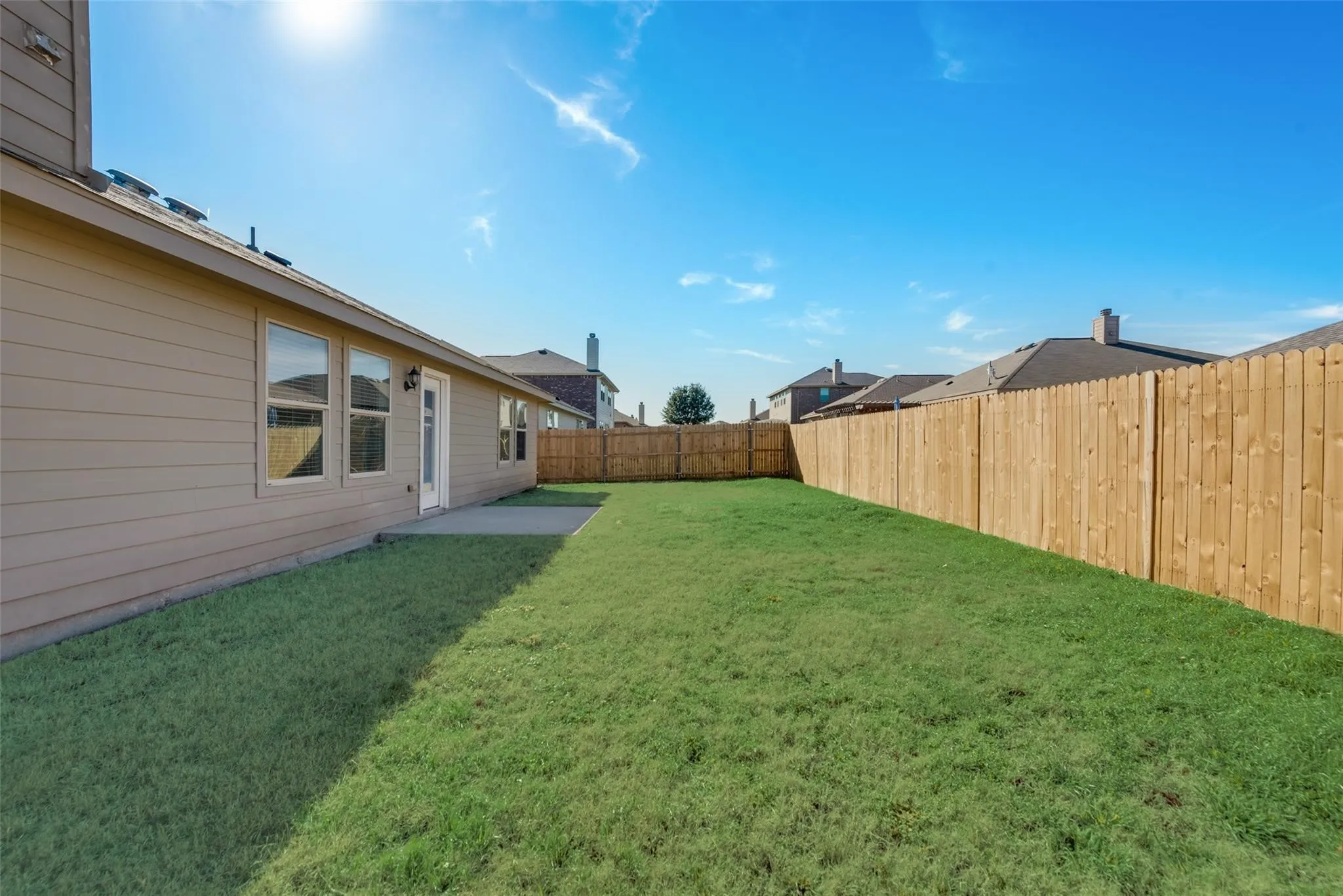 Expansive backyard featuring a lush lawn, concrete patio, and full wood privacy fencing